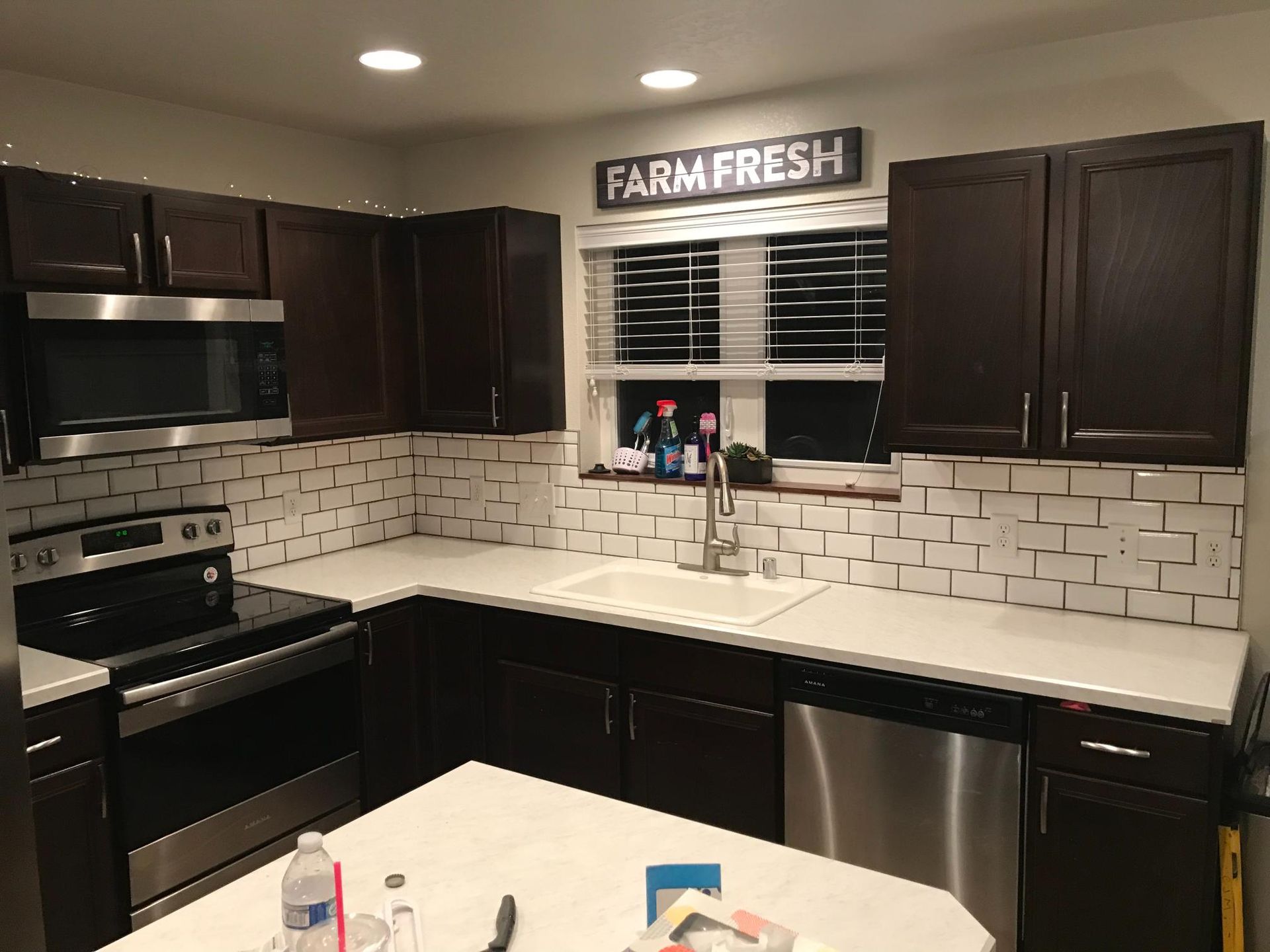 Dark brown kitchen cabinets with white backsplash, countertops, and stainless steel appliances.