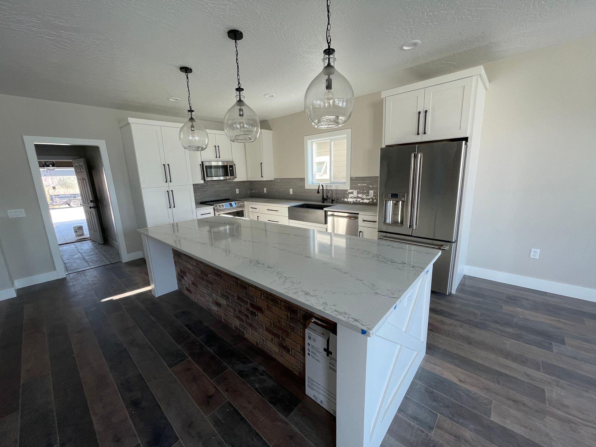 Modern kitchen with white cabinets, island, stainless steel fridge, and wooden floors.