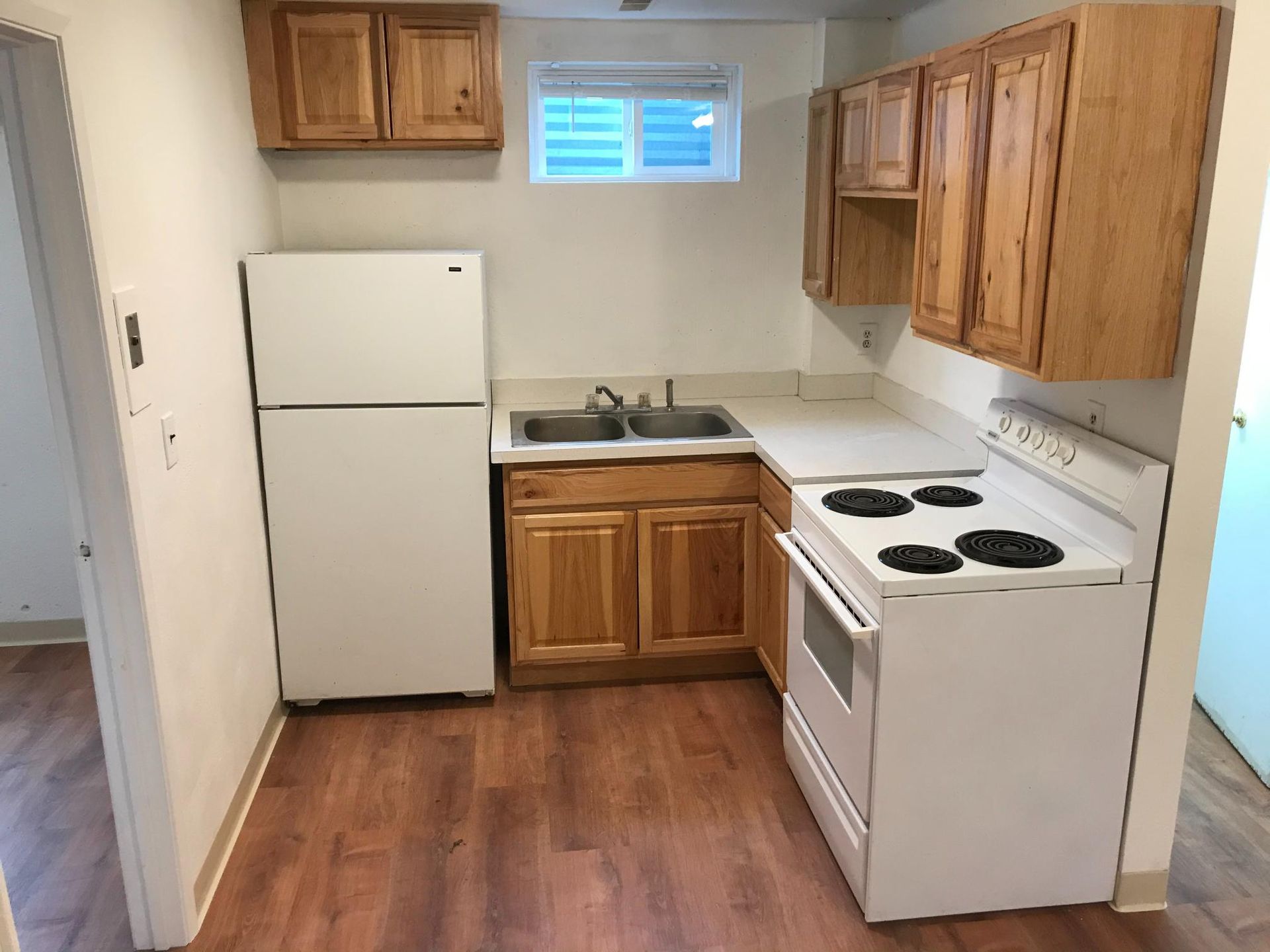 Small kitchen with white appliances, wooden cabinets, and laminate flooring.