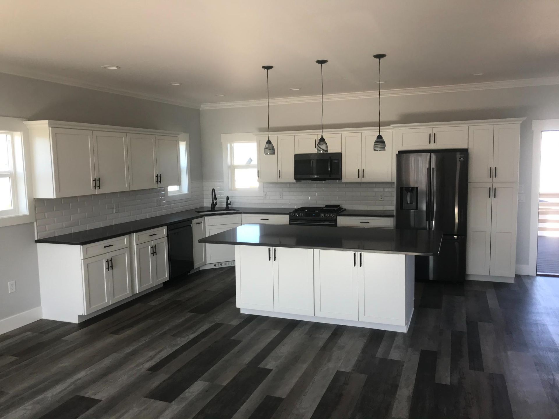 Modern white kitchen with black countertops and appliances, island, dark wood floor.