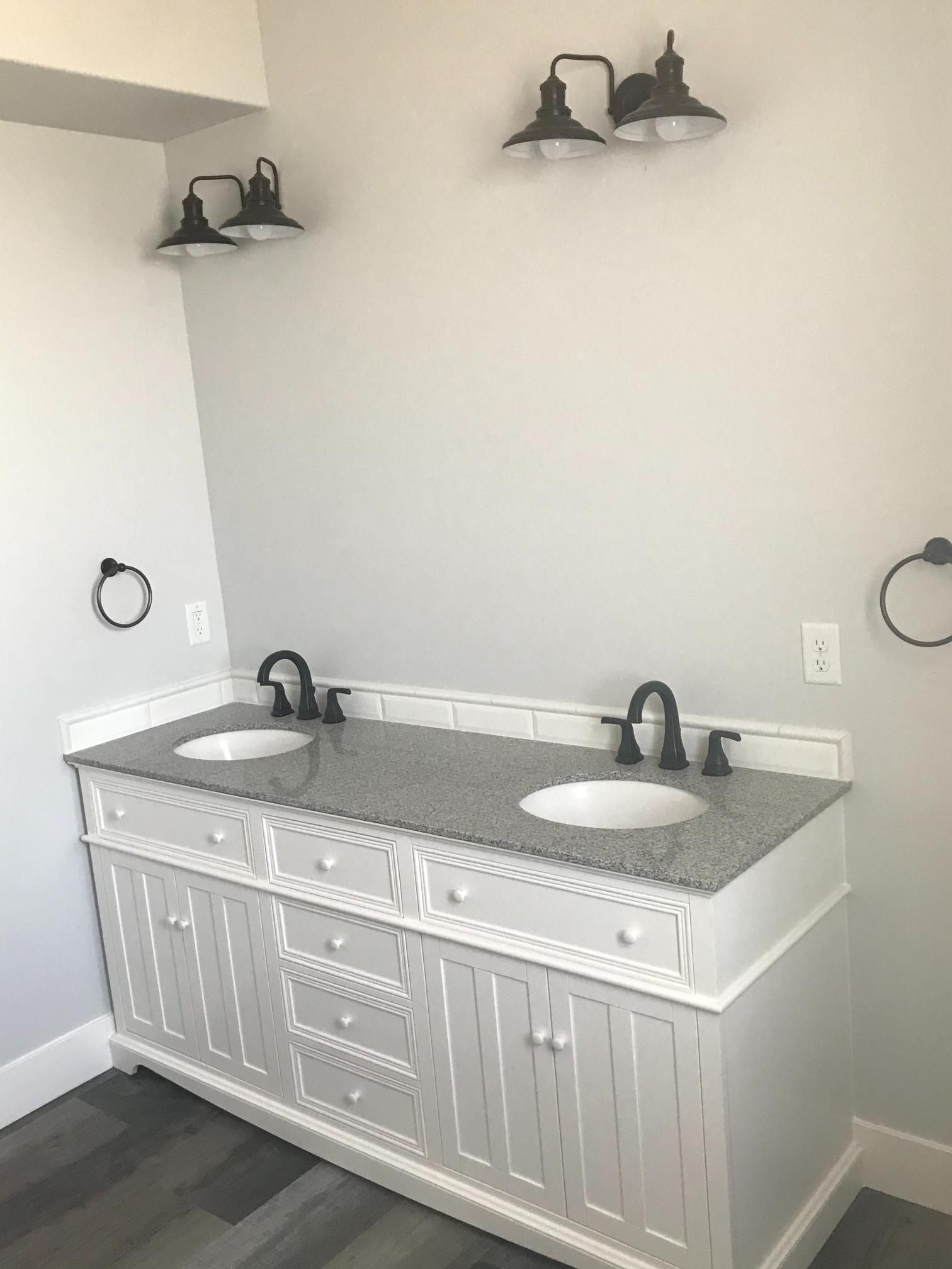 Bathroom with a white vanity, two sinks, granite countertop, and gray walls, with two sets of black light fixtures.