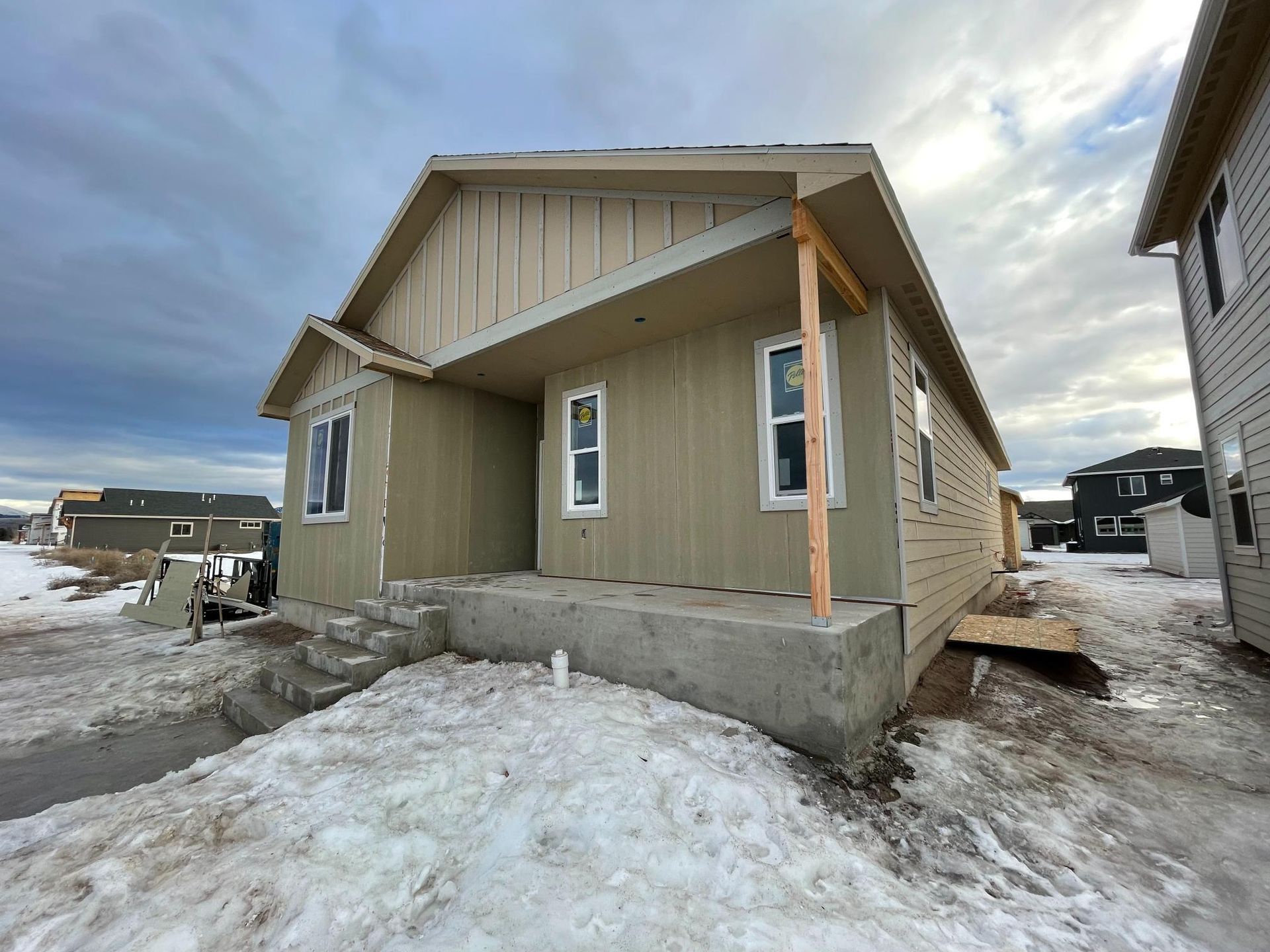 A light brown house under construction with snow on the ground, cloudy sky.