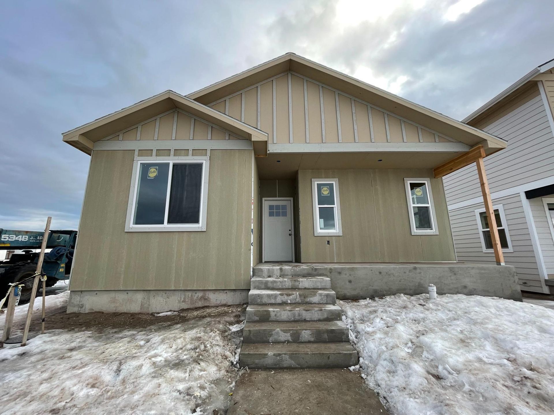 Beige house under construction, with snow-covered ground and concrete steps leading to the front door.