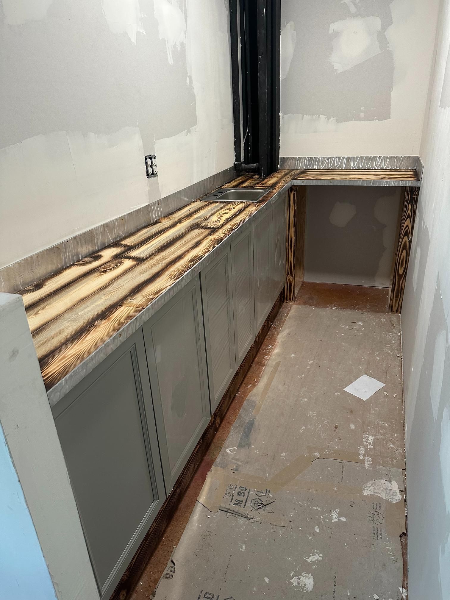 Unfinished room with gray cabinets, a stained countertop, and black pipe against white walls.