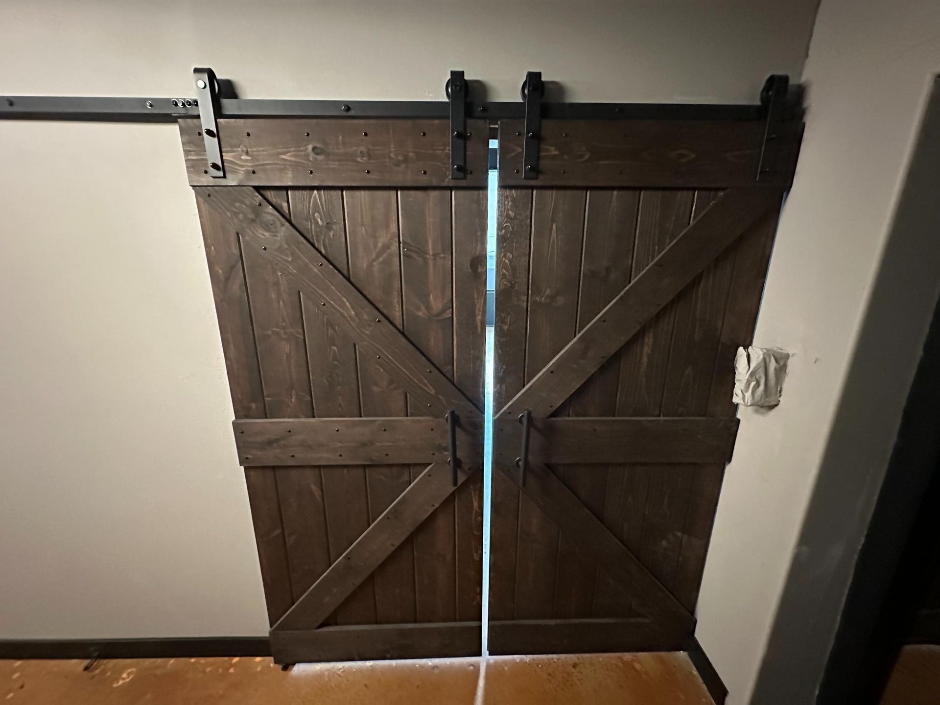 Dark wood double barn doors on a black track, with a gap showing light.