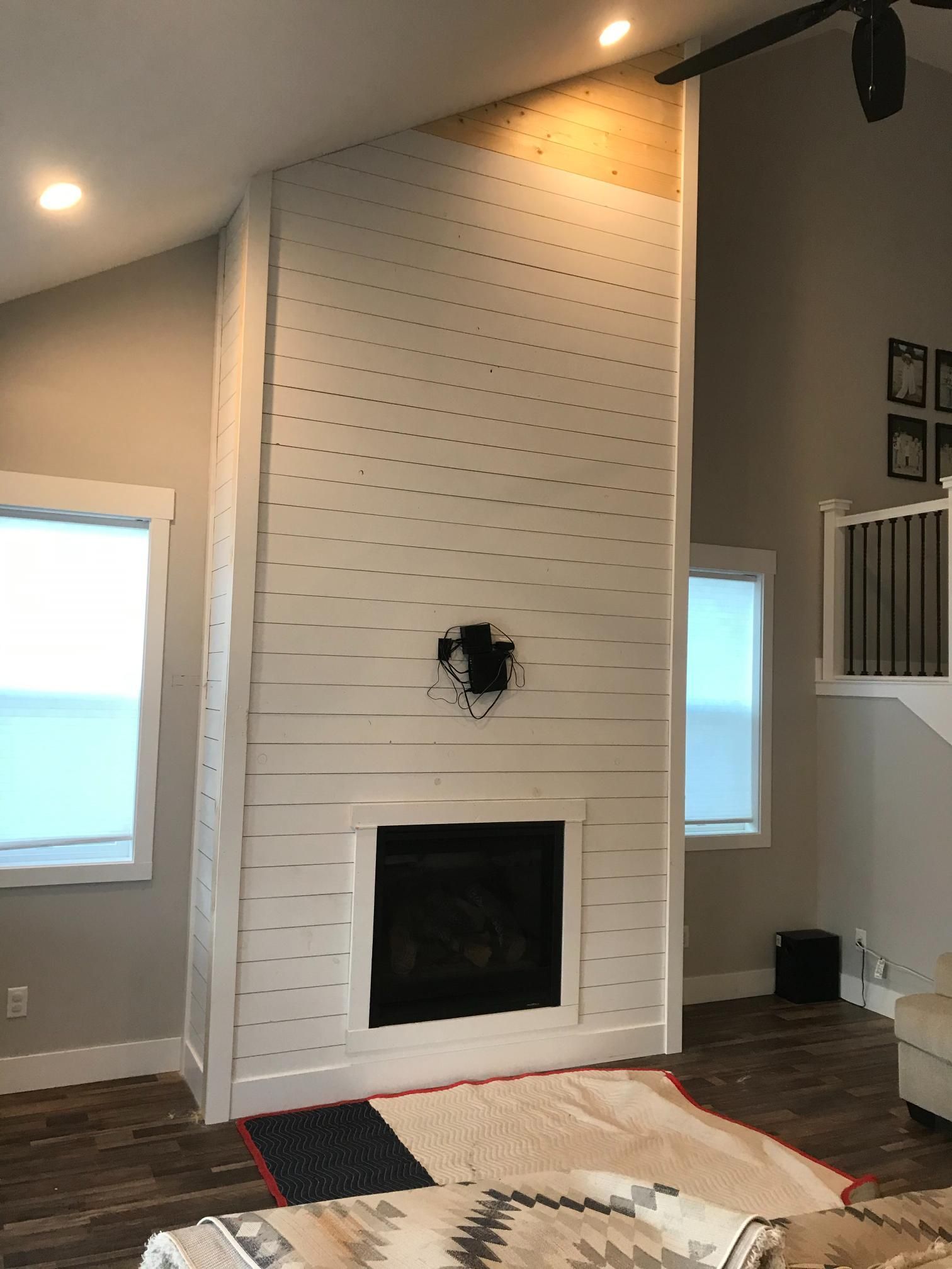White shiplap fireplace with dark interior, flanked by windows. Wooden floors, tan walls.