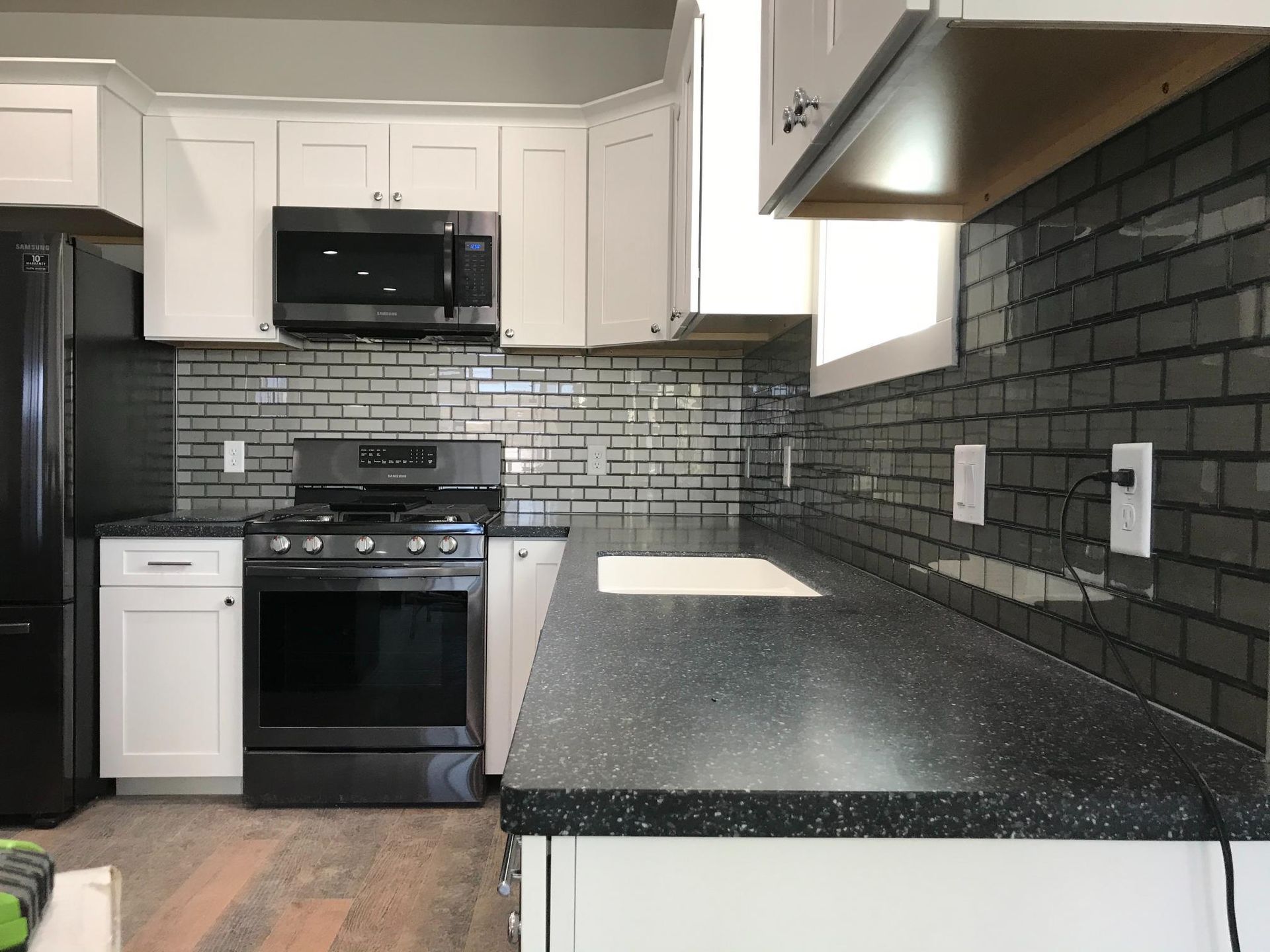 Kitchen with black appliances, white cabinets, and gray brick backsplash.