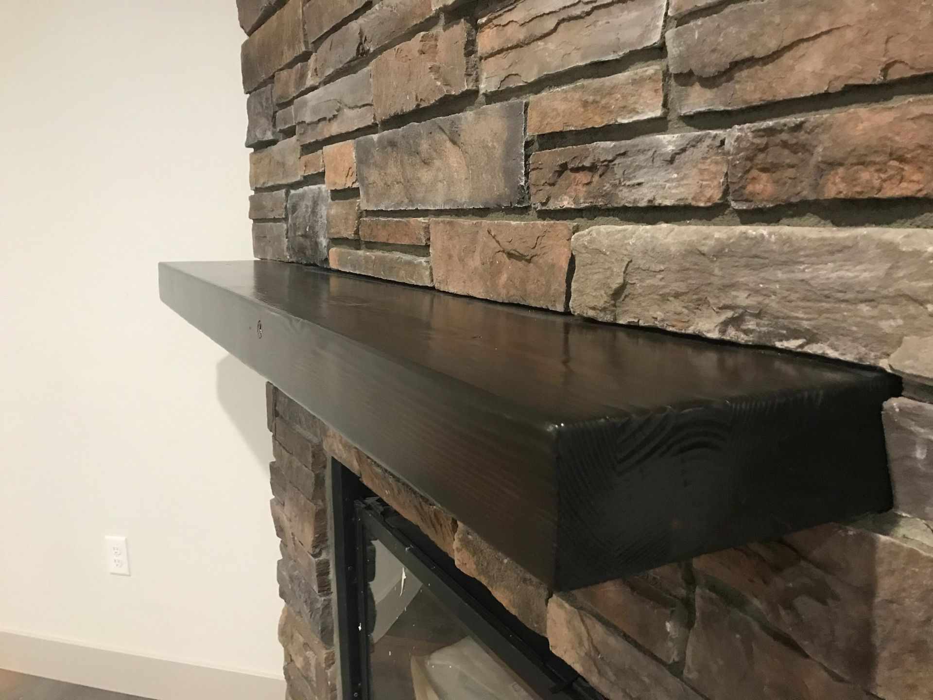 Black wooden fireplace mantel against a stone wall.
