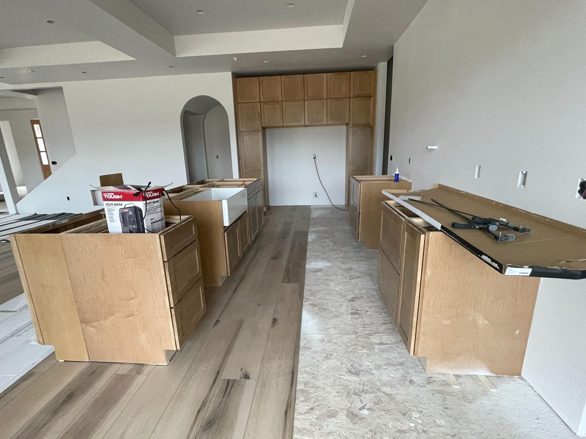 Kitchen under construction with unfinished cabinetry, hardwood floors, and drywall.
