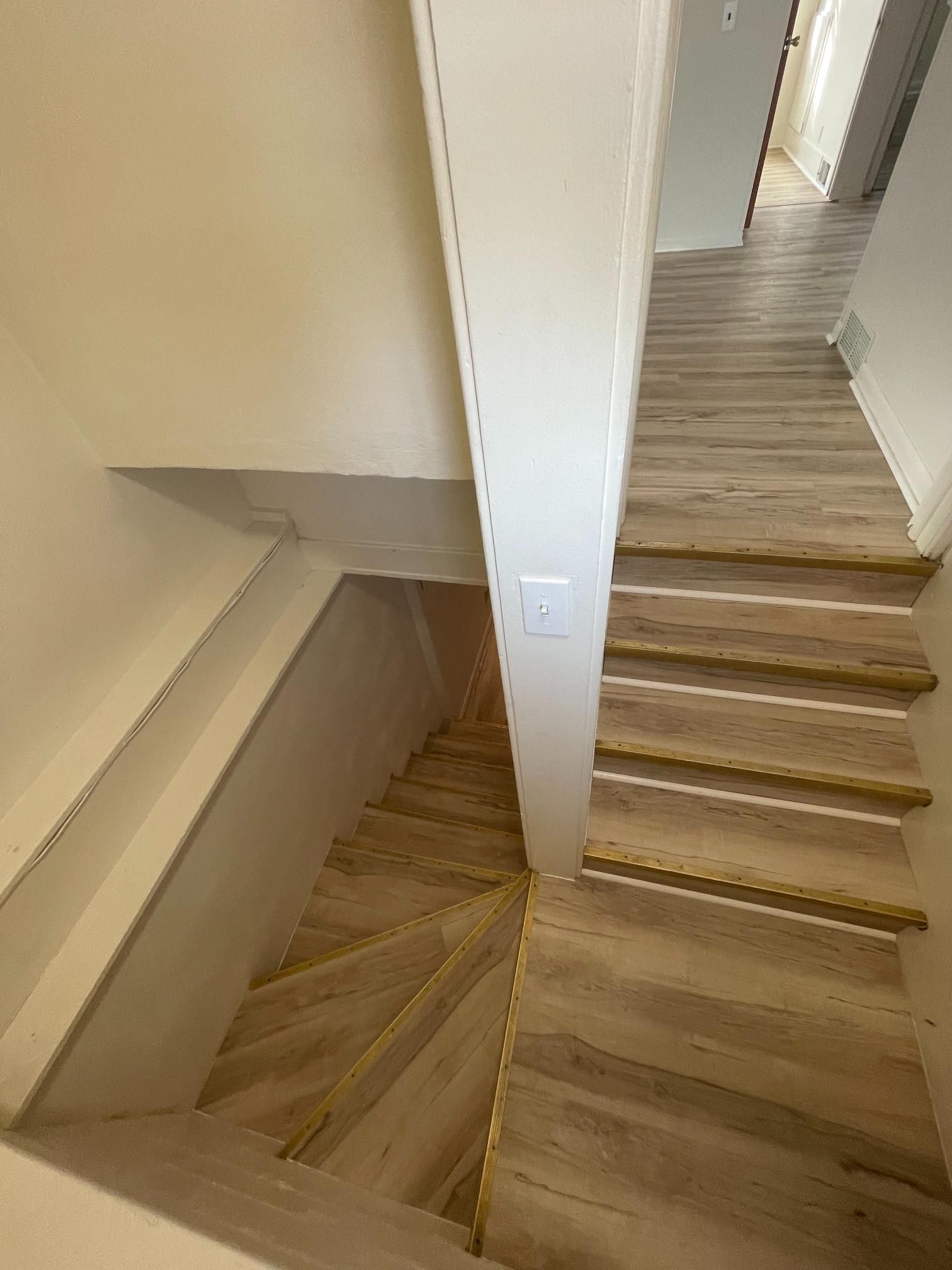 Staircase with light wood steps leading down, with a white wall and handrail.