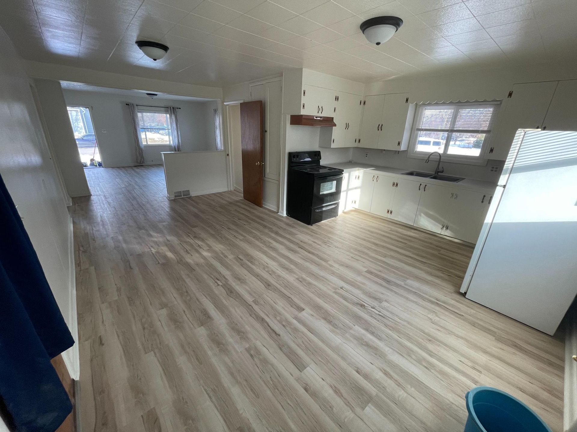 Interior of a home with light-colored flooring, kitchen with white cabinets, and living area.