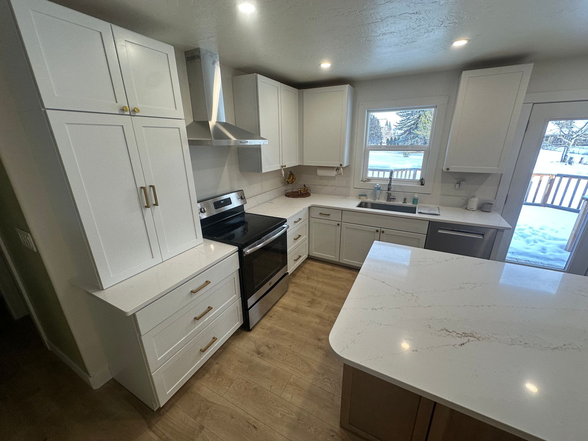 White kitchen with island, cabinets, stove, and sink. Light wood floor.