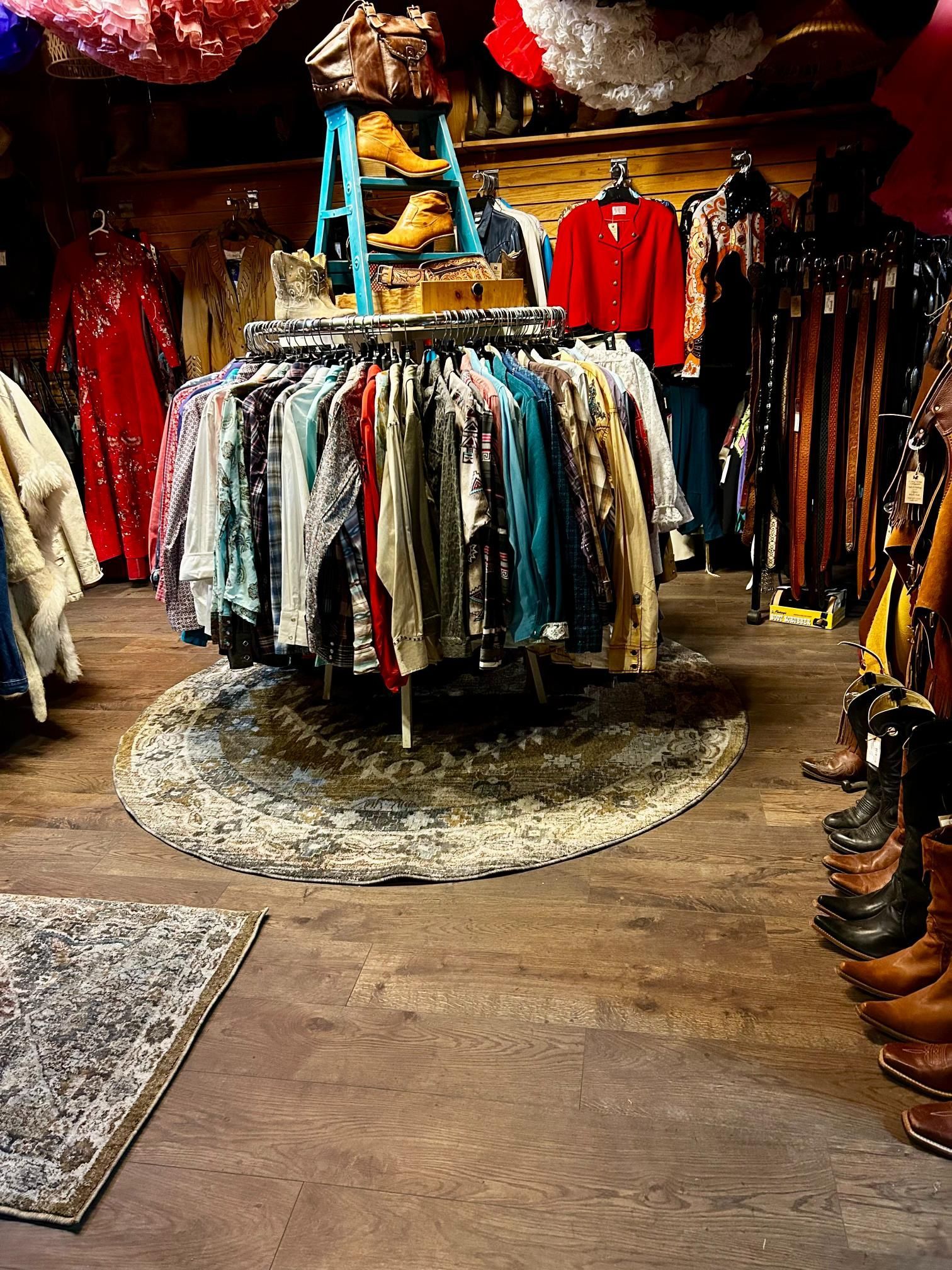 Clothing racks in a vintage shop. A teal ladder holds boots. Clothes in bright colors are displayed.