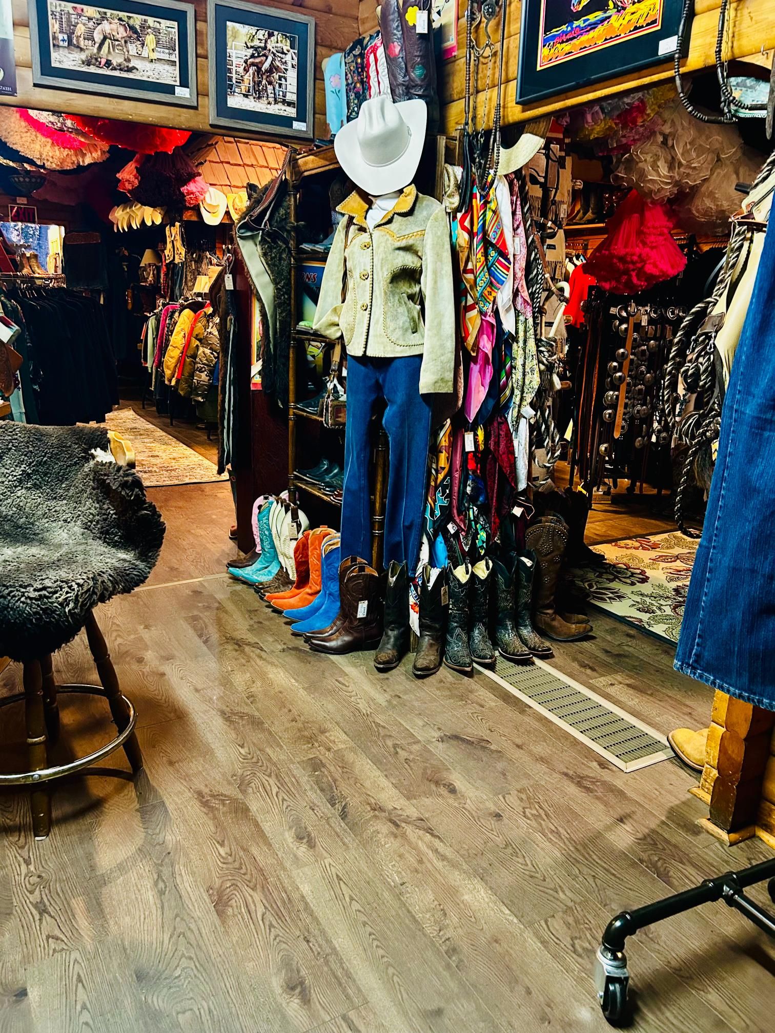 Inside a Western-themed clothing store; mannequin in jacket and jeans, boots lined up, clothes racks.