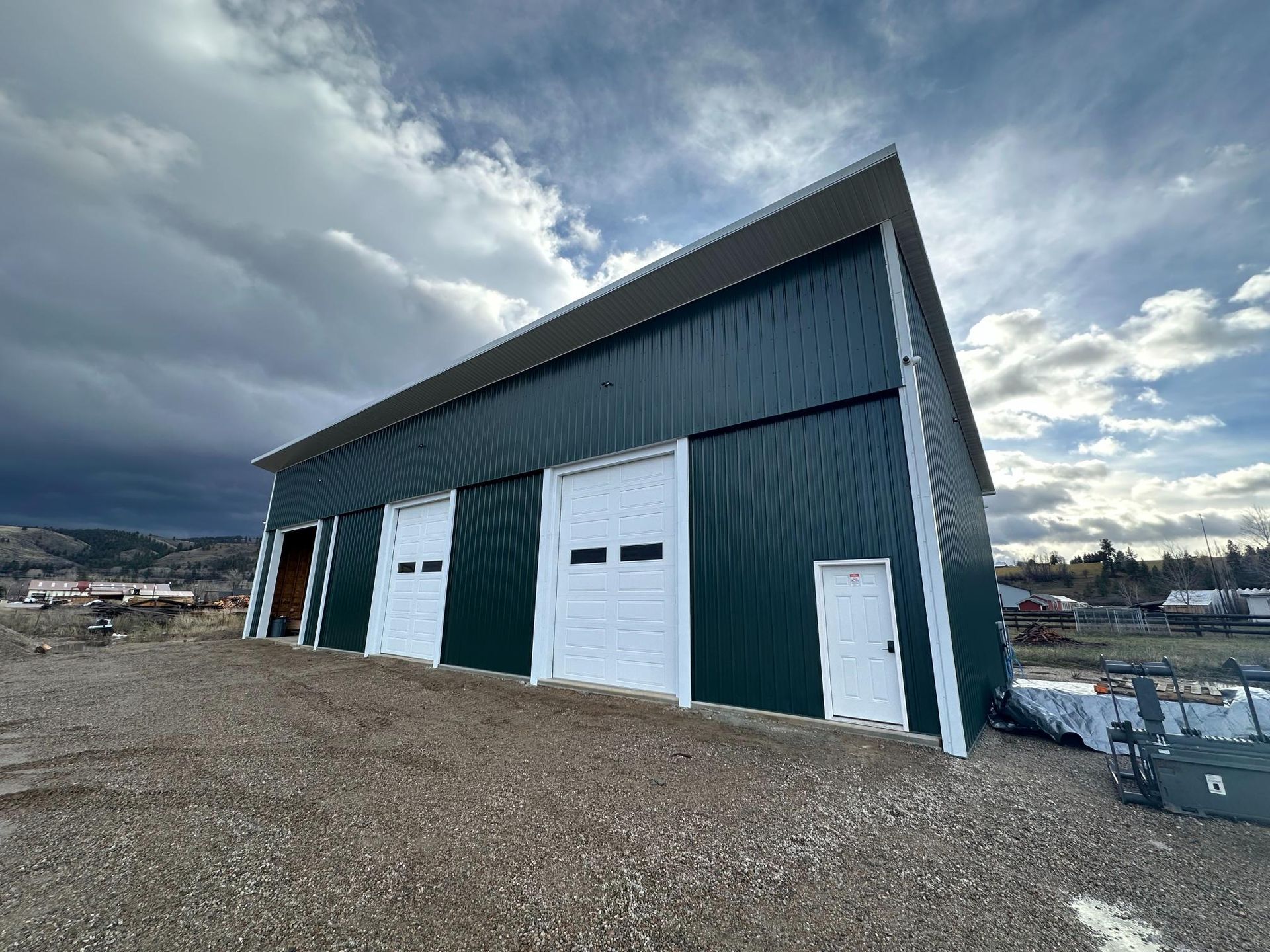 Green metal warehouse with white doors under a cloudy sky.