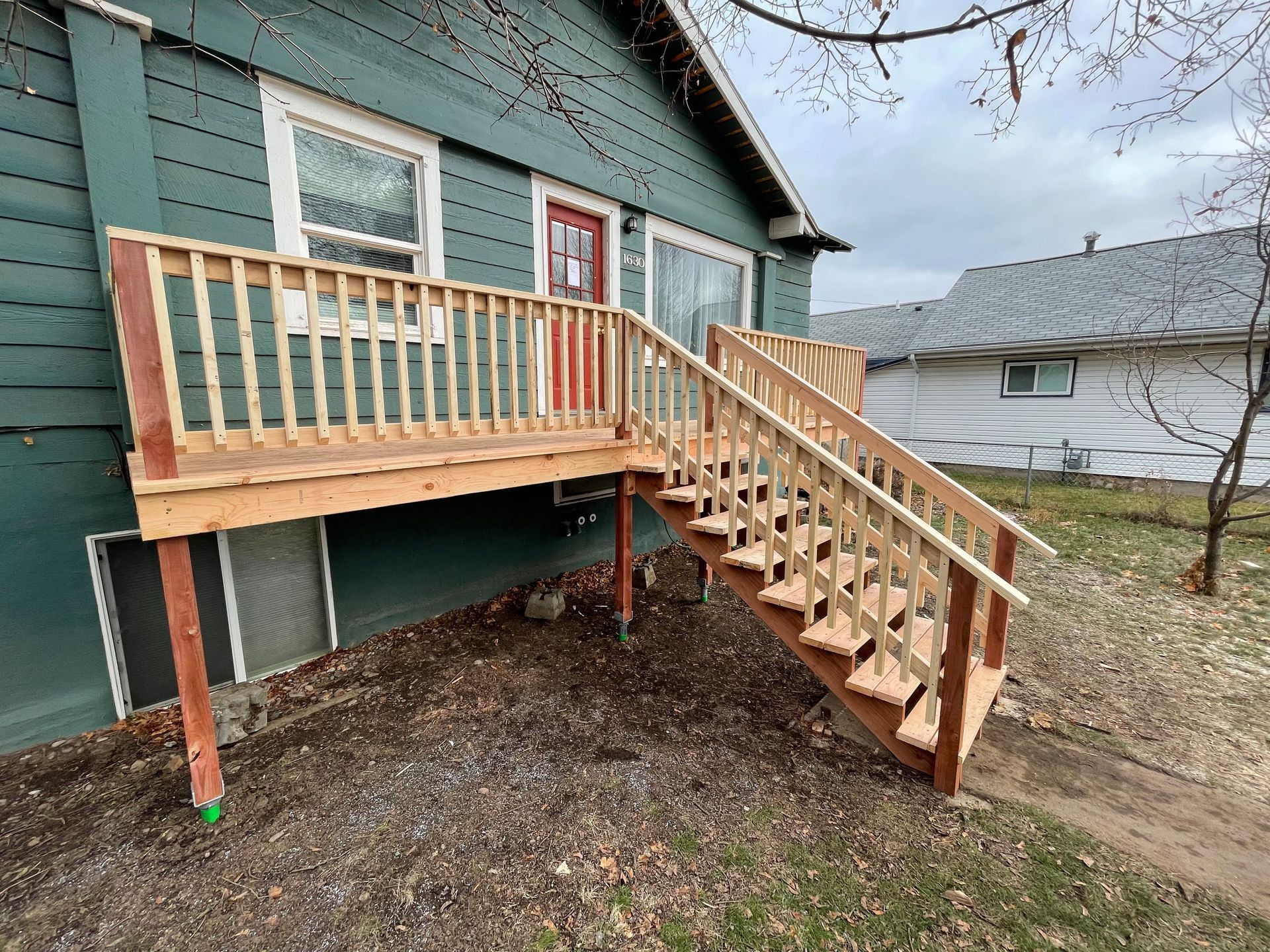 Wooden deck with stairs attached to a teal house, brown railing and door.