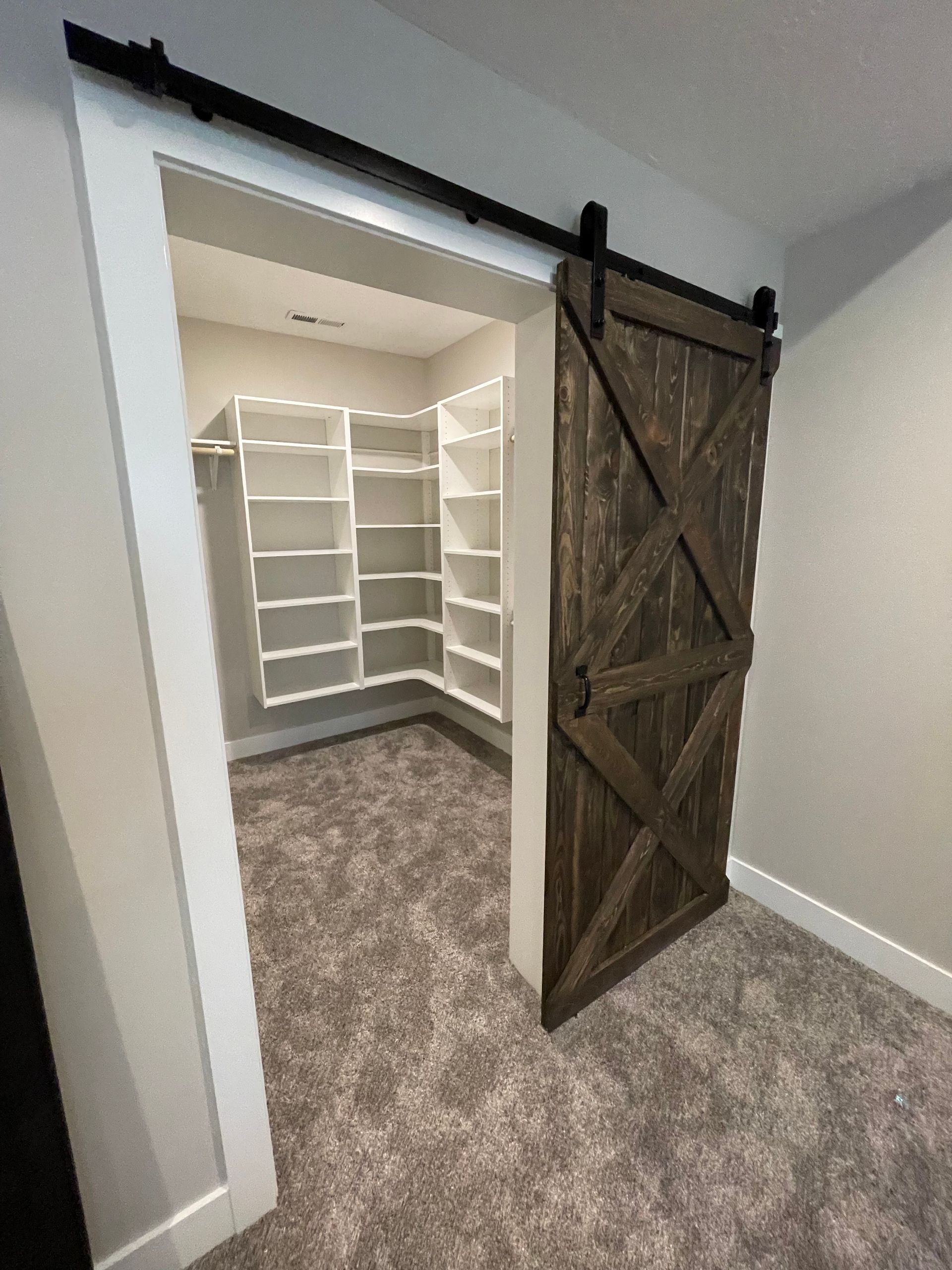 Wooden barn door open to a walk-in closet with white shelves and gray carpet.