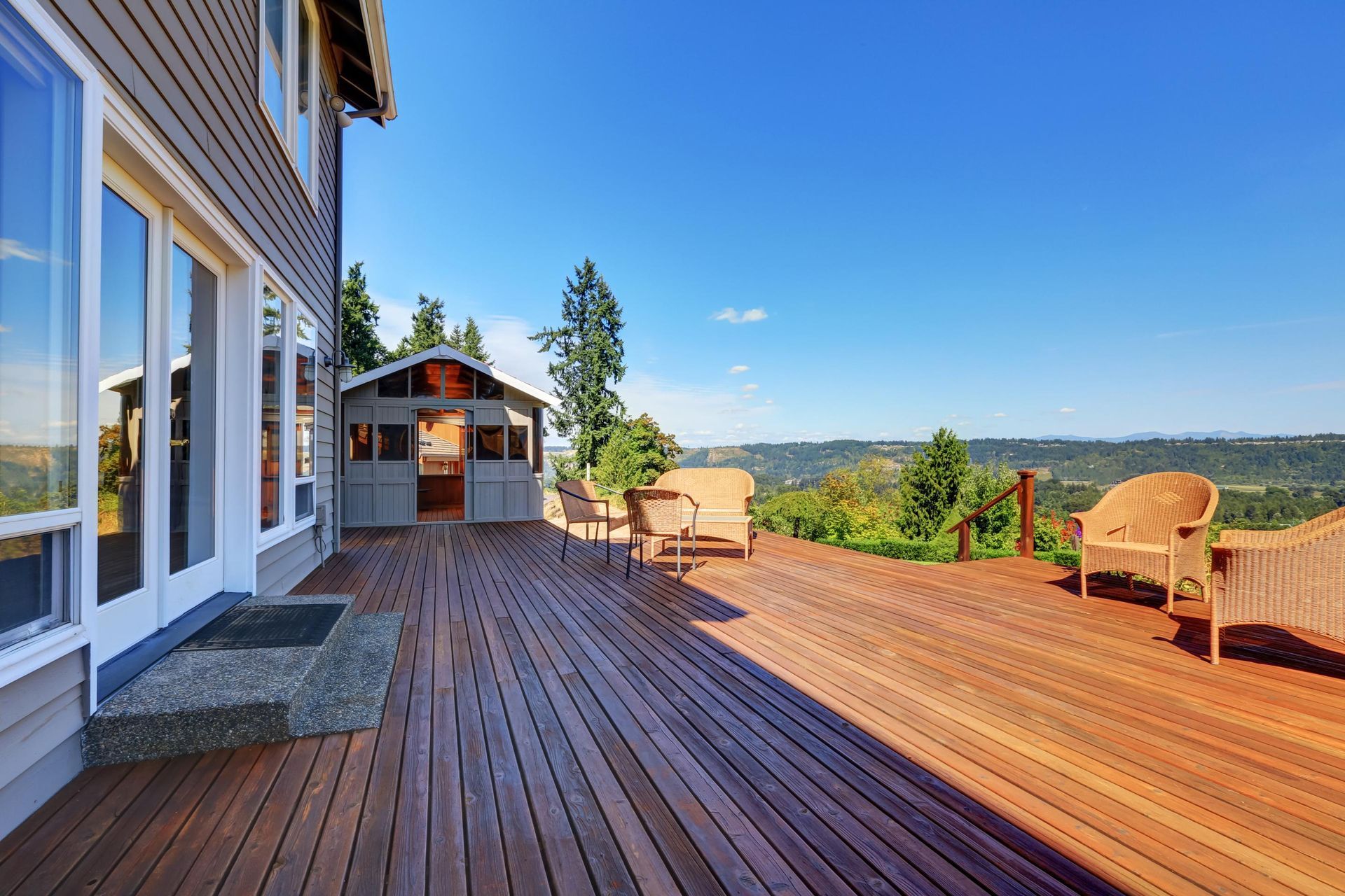 Wooden deck with seating and small building overlooking a green landscape under a blue sky.