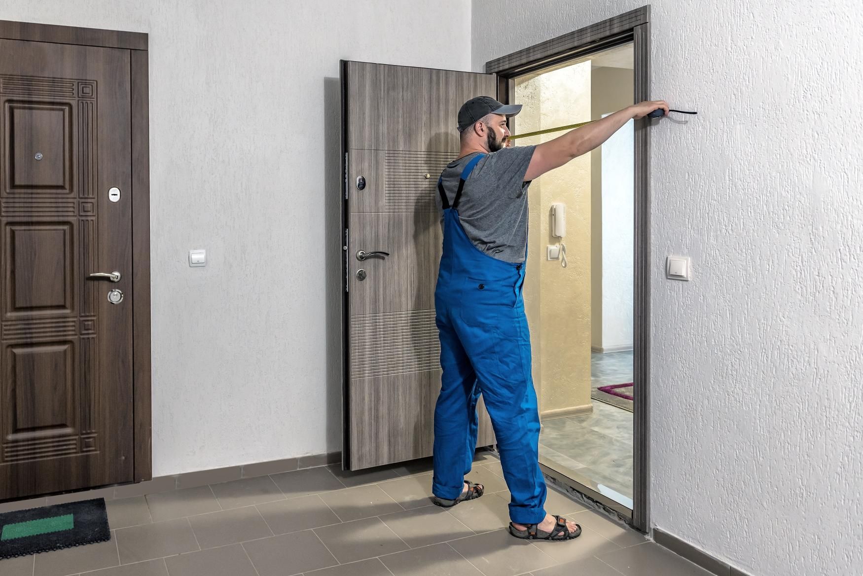 Person in blue overalls measuring a door frame in an interior setting.