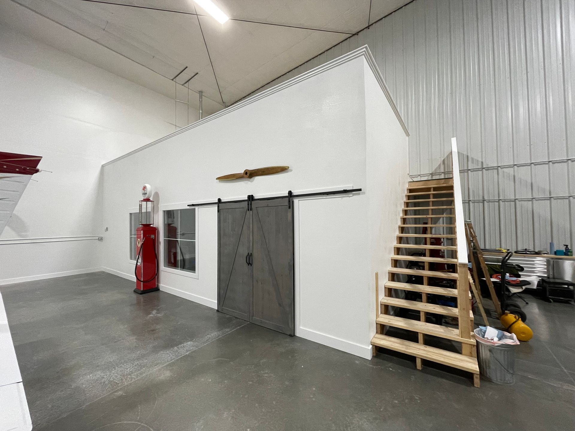Interior of a warehouse with a white office structure, gray sliding barn door, and wooden stairs.