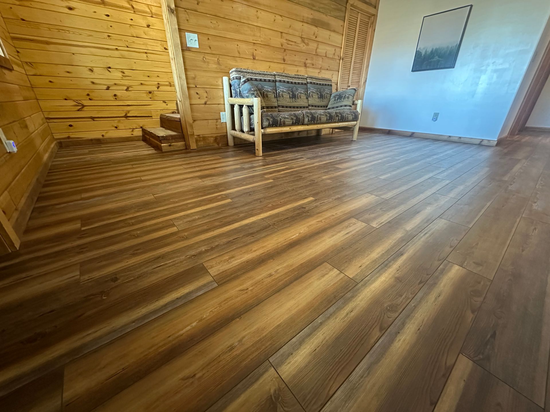 Wooden floor in a room with wood paneling and a couch.
