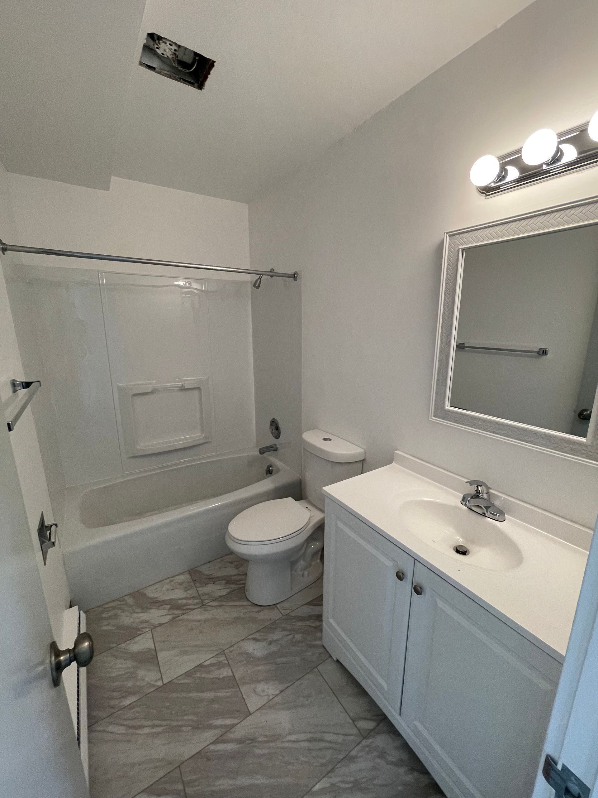 White bathroom with a tub, toilet, vanity, and gray tile floor.