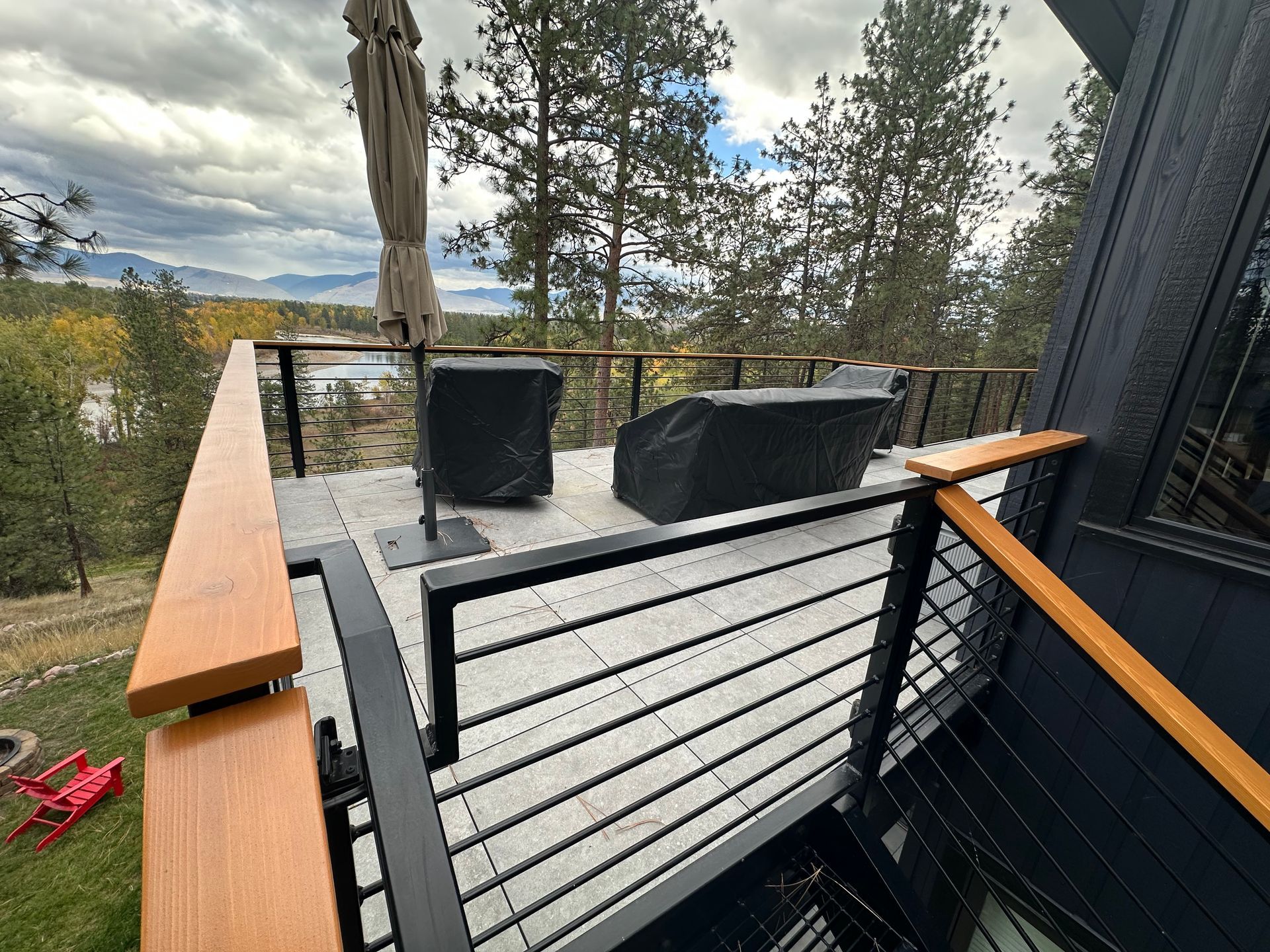 Deck with black railing, light wood handrails, and covered outdoor furniture overlooking a scenic view.