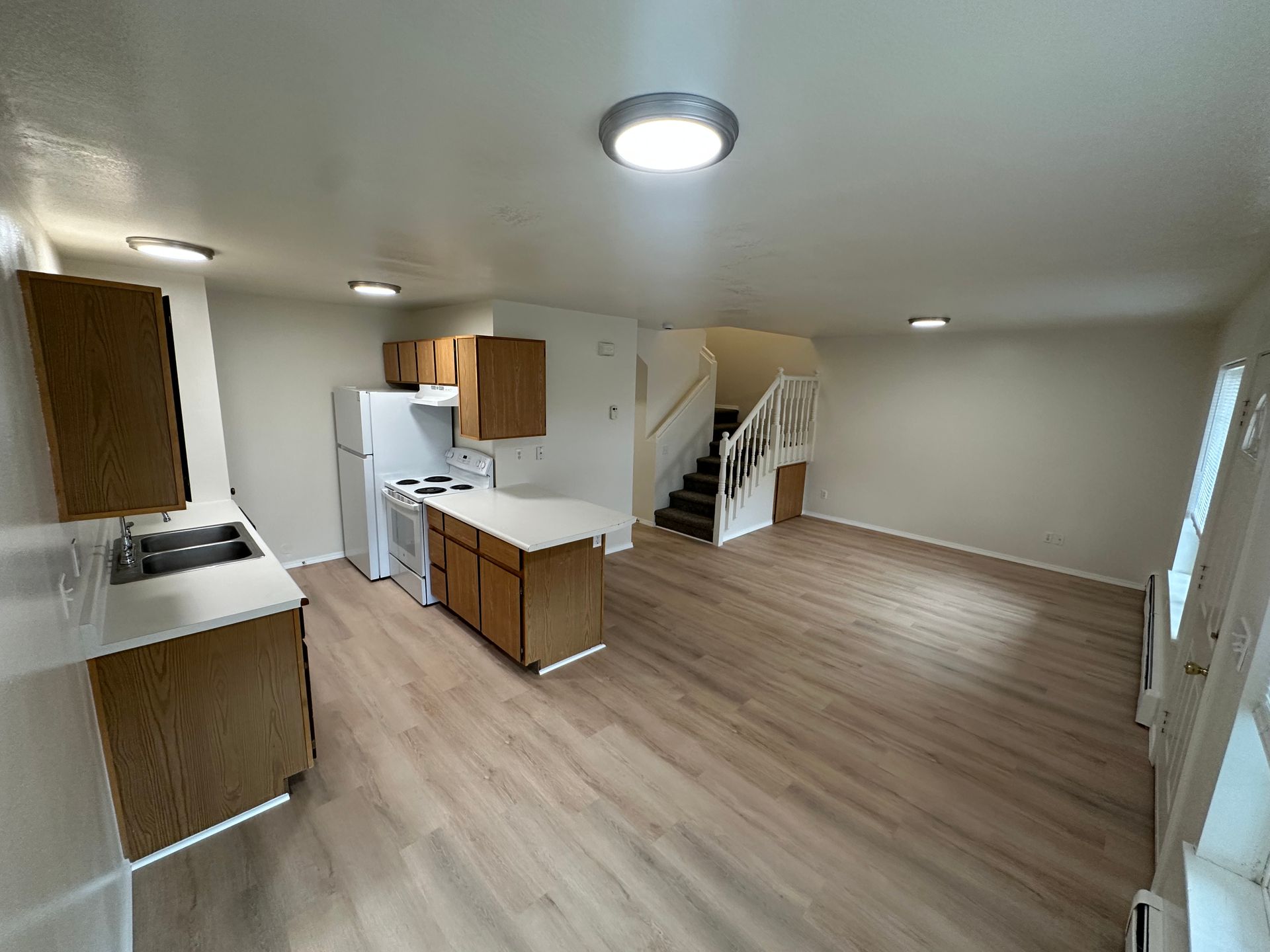 Open-concept apartment with kitchen, living space, and stairs leading up. Light wood flooring and neutral walls.