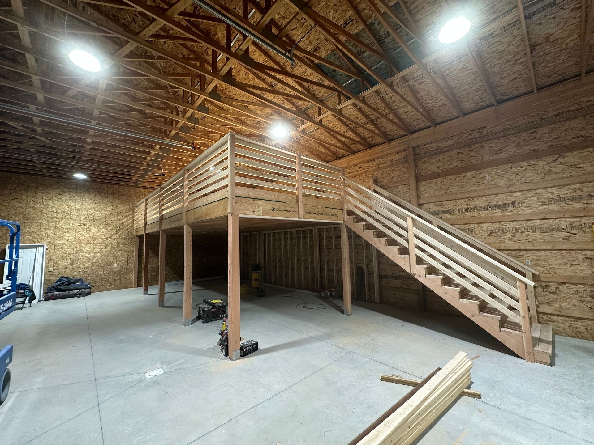A wooden mezzanine with stairs inside a large industrial building, illuminated by overhead lights.