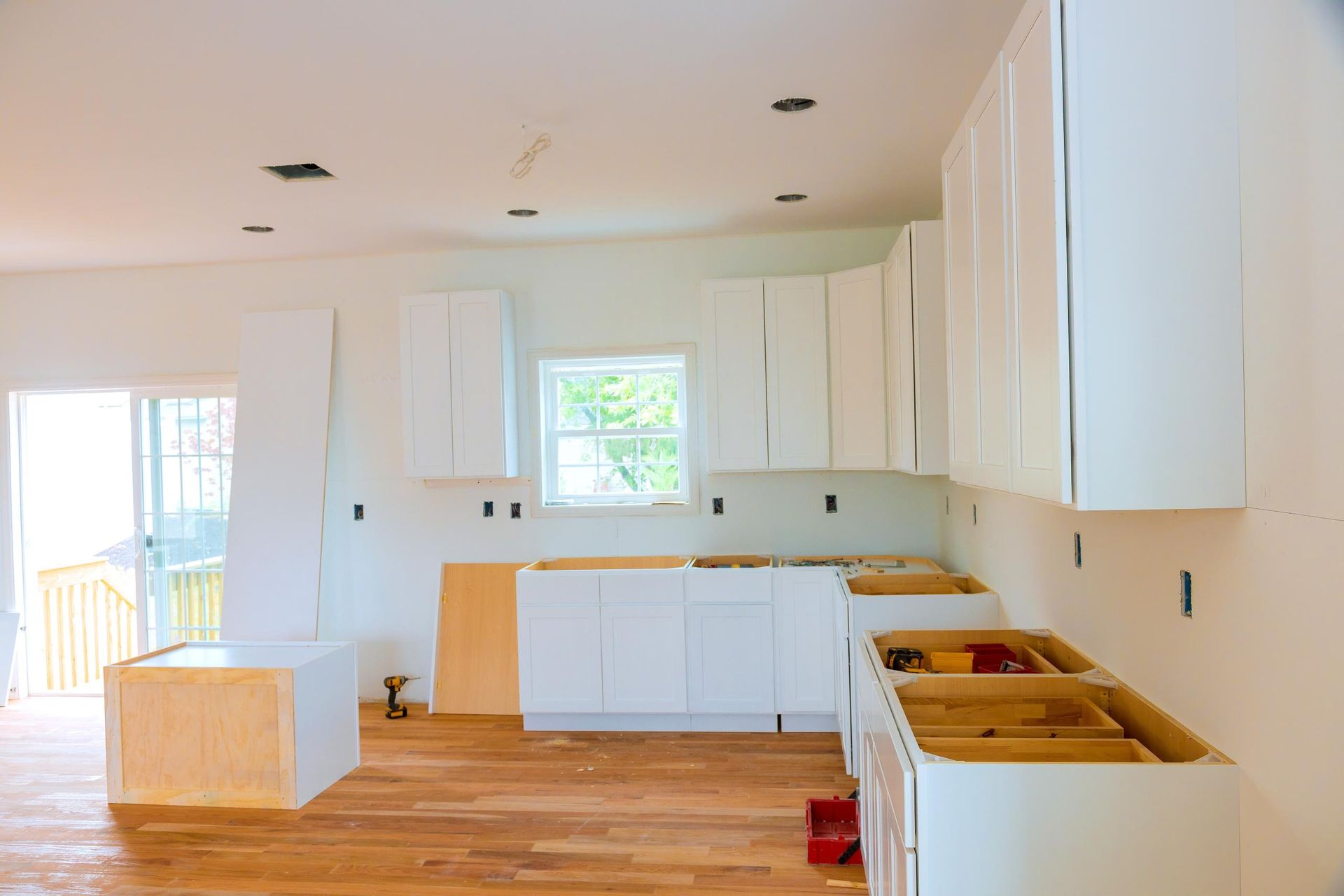 Kitchen under construction, white cabinets, wooden floors, unfinished countertops.