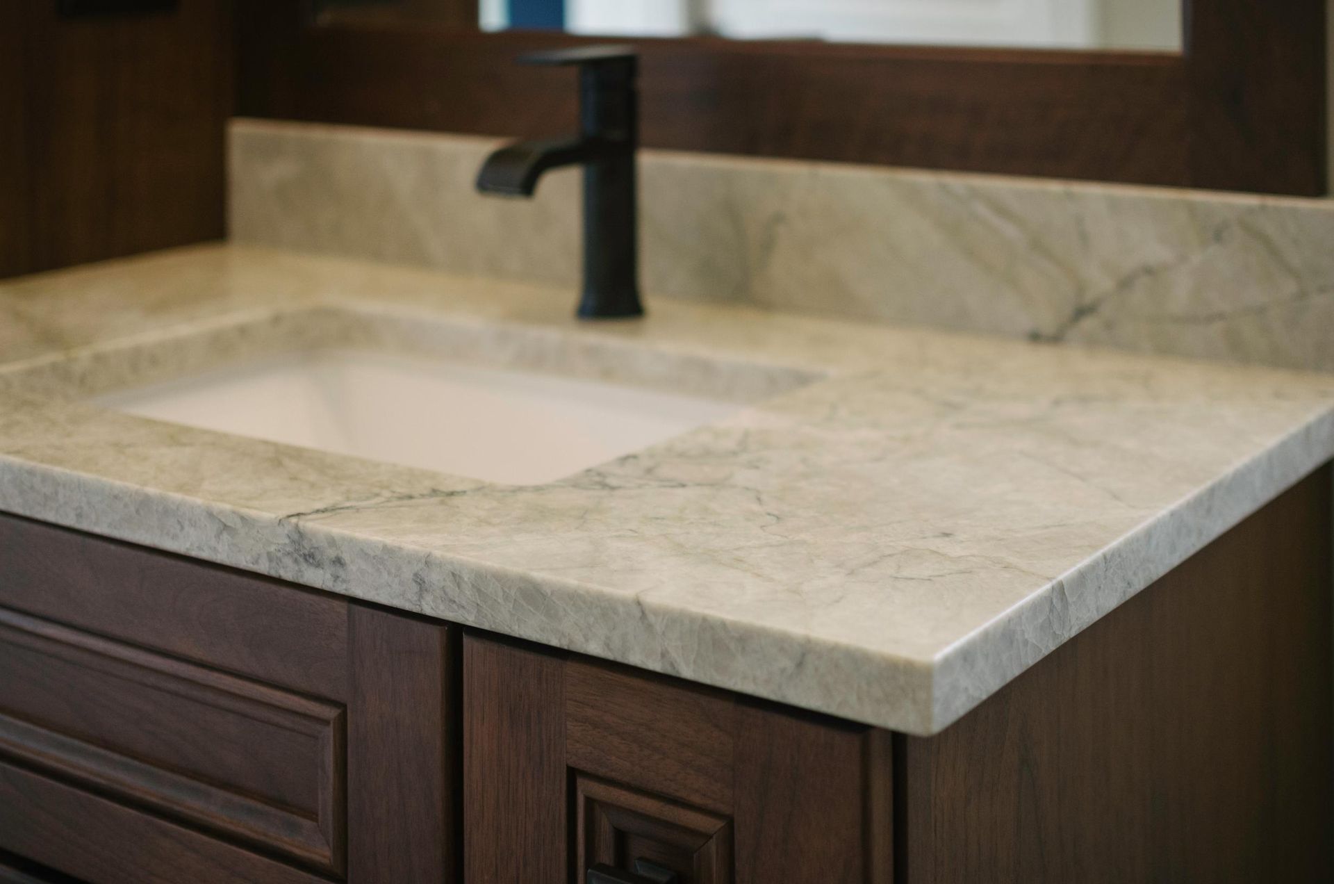 Bathroom vanity with light-colored countertop, dark faucet, and wood cabinetry.