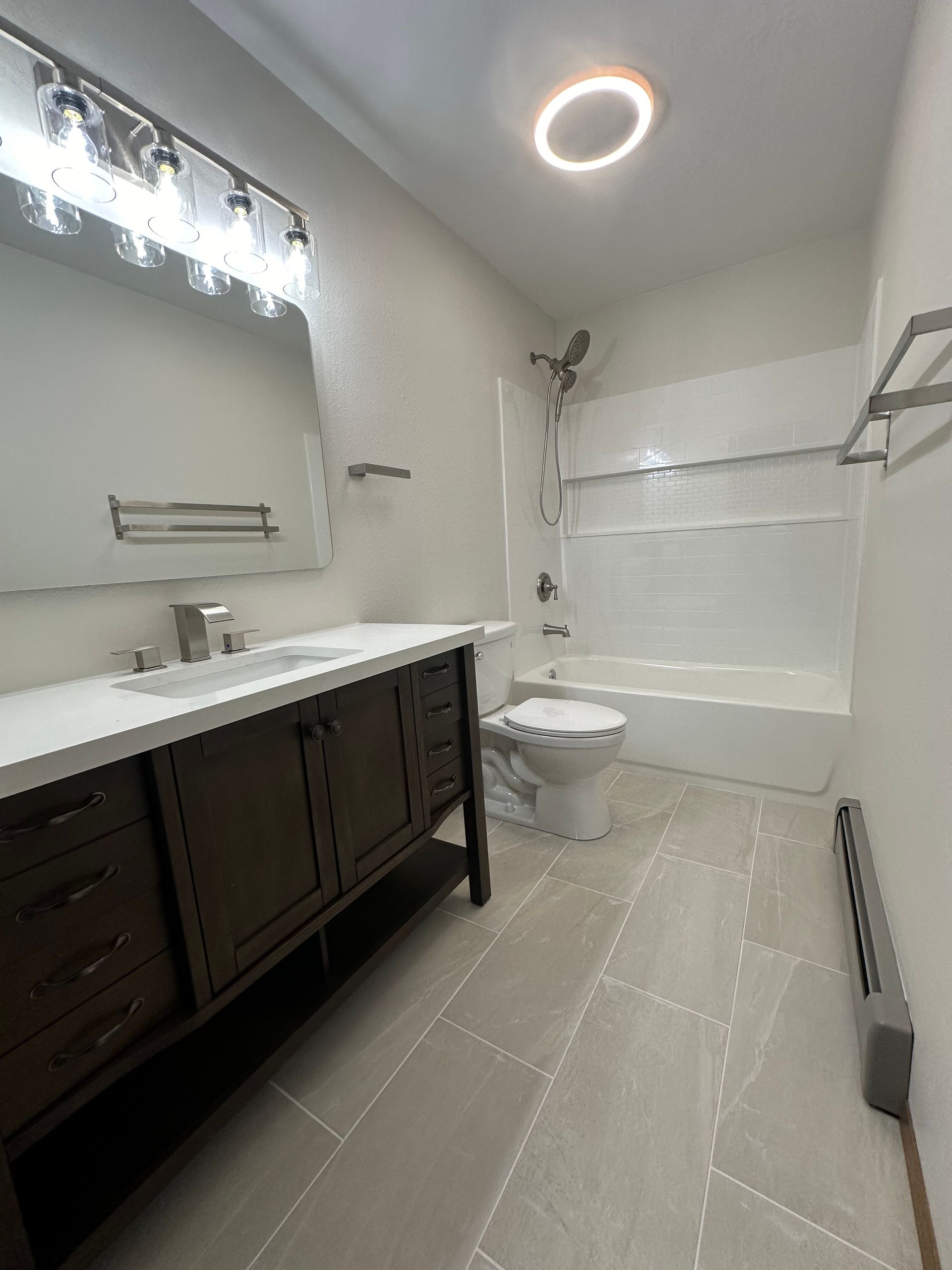 Bathroom with dark brown vanity, white countertop, and tiled floor. Shower/tub combo.
