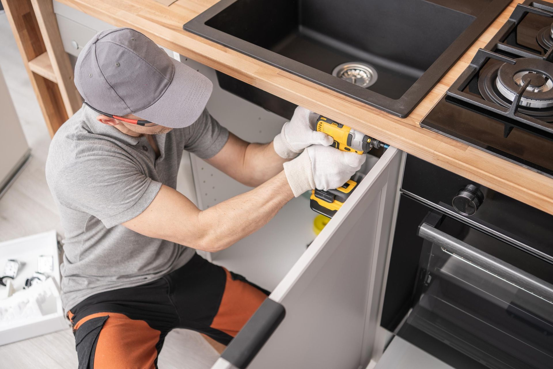 Man installing a cabinet door with a drill in a kitchen.