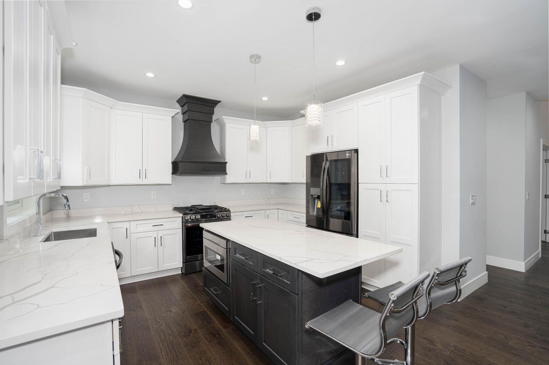 Modern kitchen with white cabinets, dark island, black hood, stainless steel appliances, and dark wood floors.