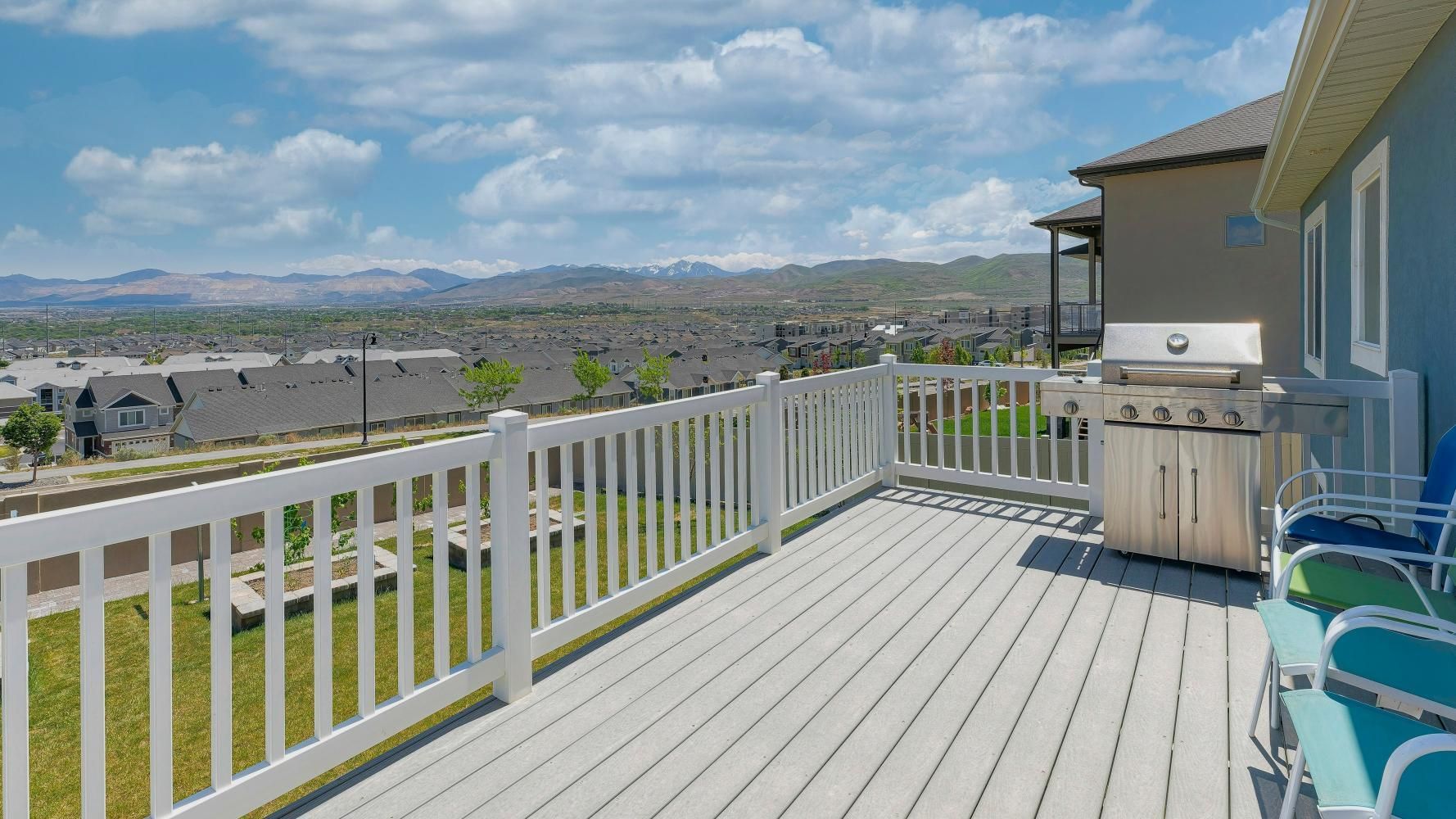 Deck with white railing and grill, overlooking a landscape with houses and mountains under a cloudy sky.