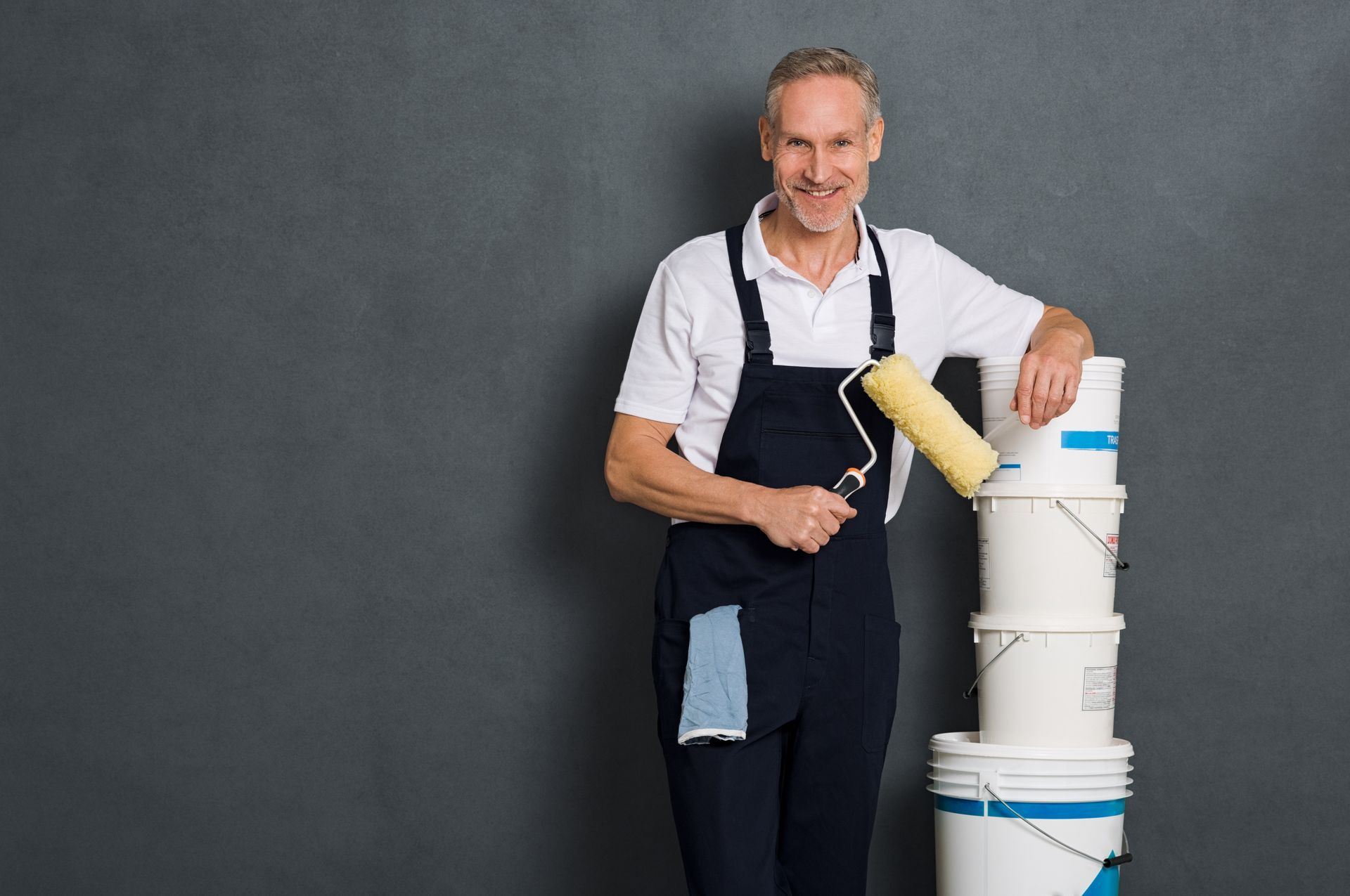 Painter holding a roller beside stacked white paint buckets against a dark gray background