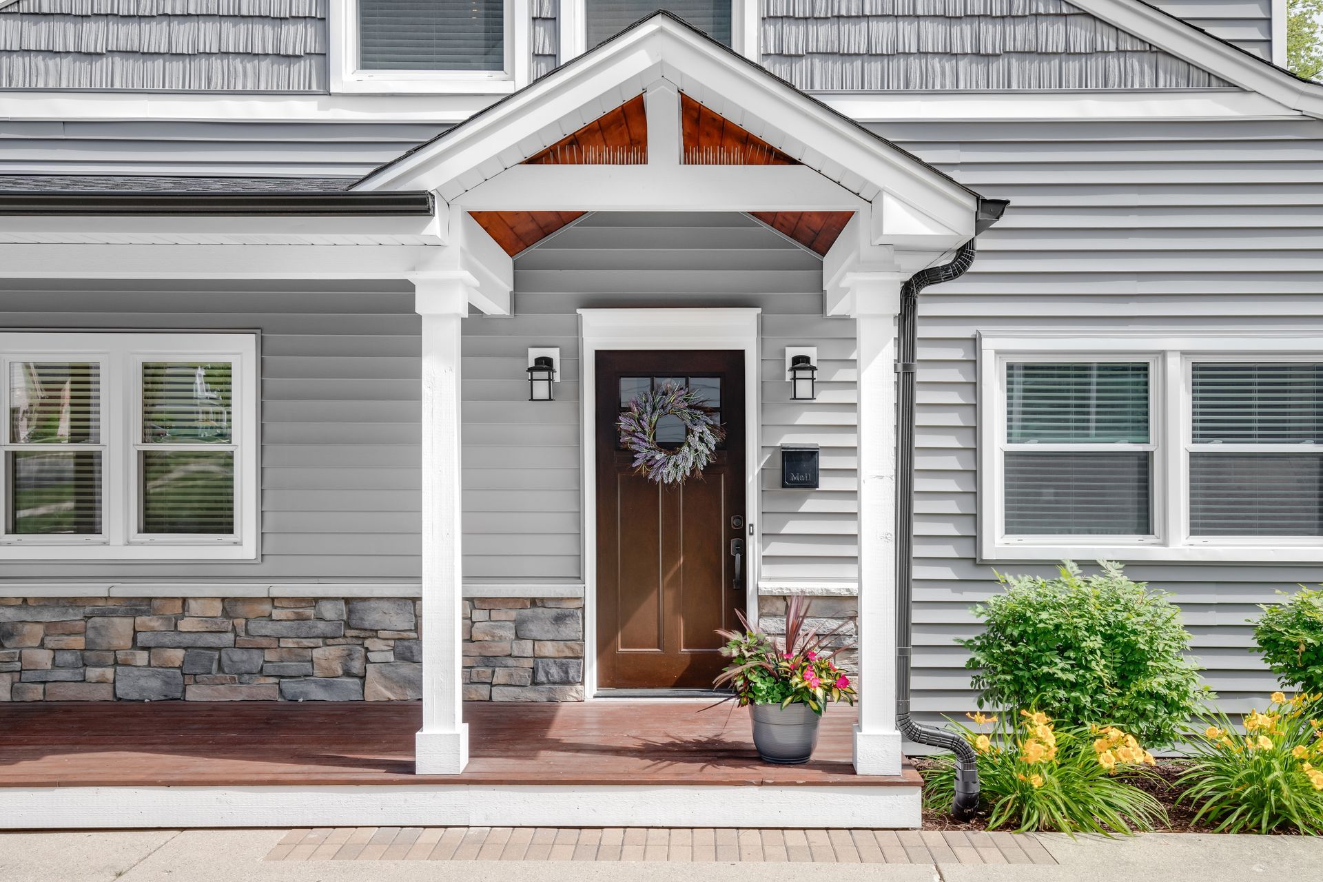 Front porch of a gray house with white trim, open front door, and potted flowers by the steps