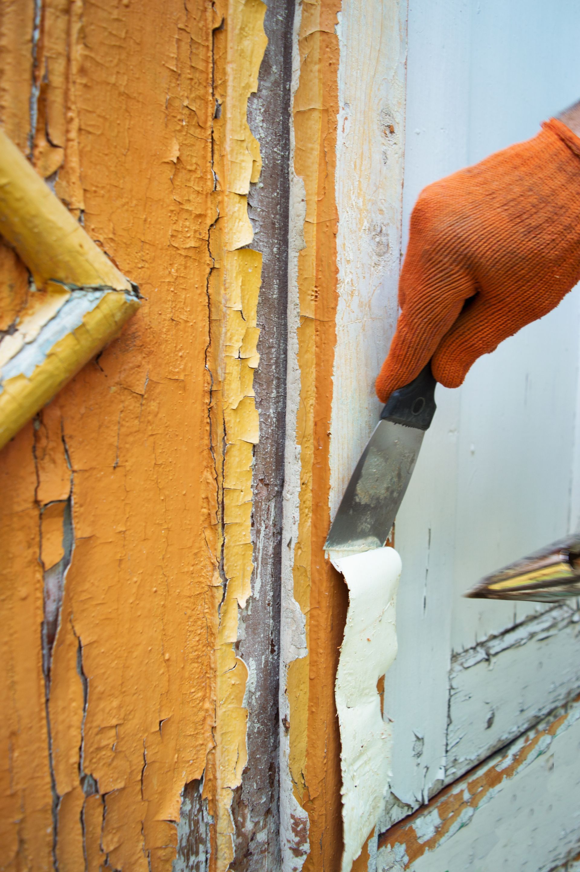 A person is peeling paint off of a door with a spatula.