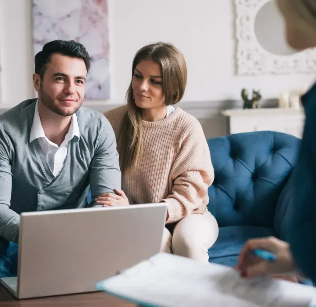 A man and a woman are sitting on a couch looking at a laptop.