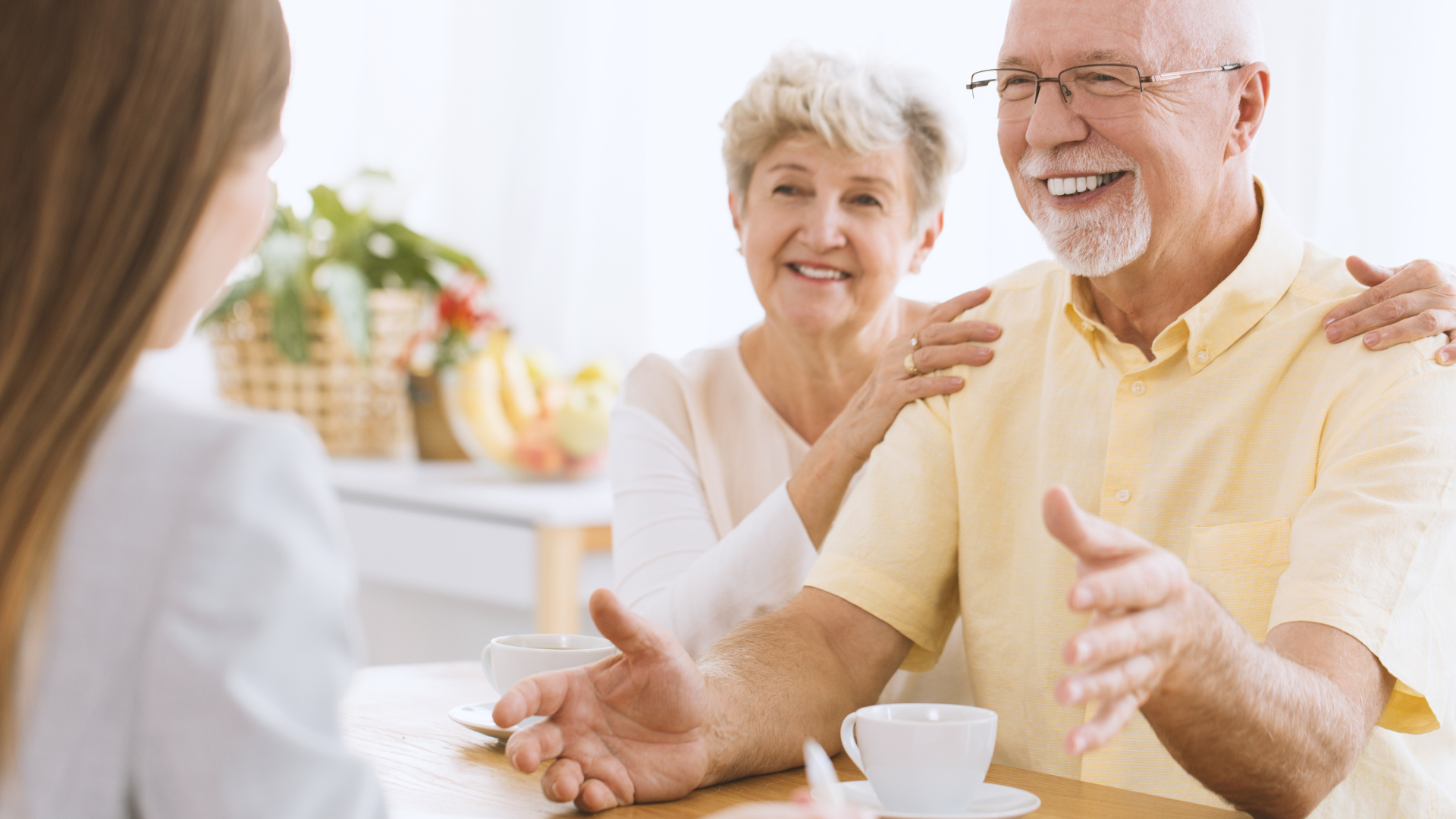An elderly couple is sitting at a table talking to a woman.