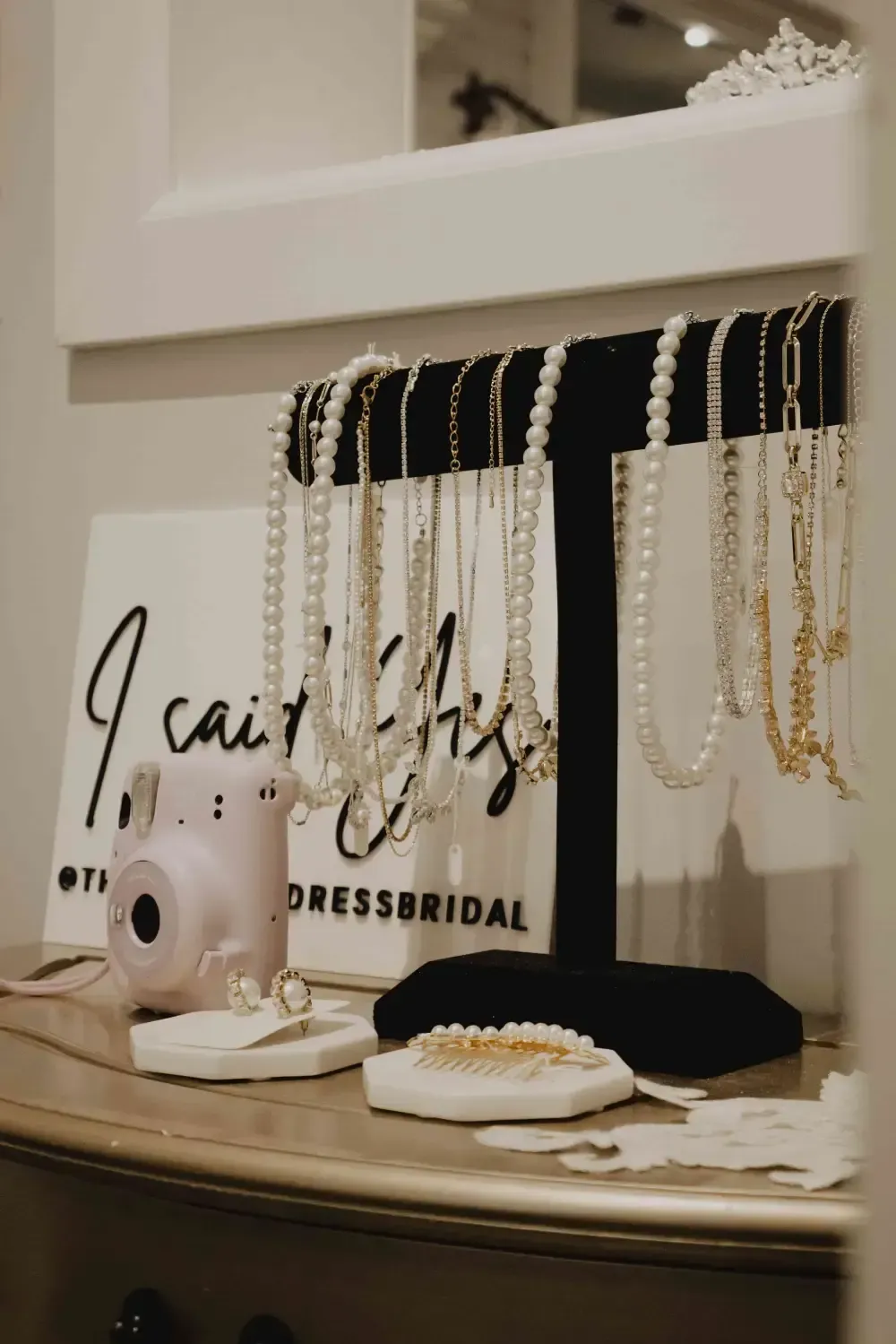 Jewelry display with necklaces, rings, and a camera on a shelf. White and gold accents.
