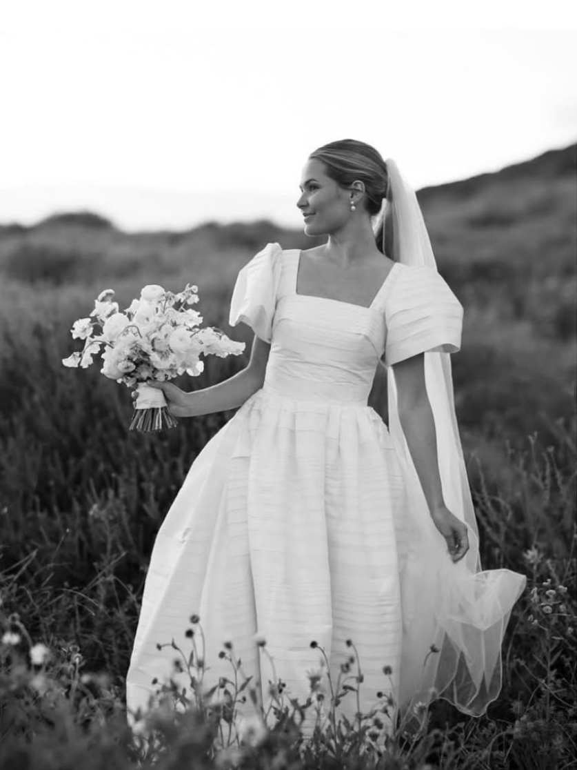 Bride in white dress, holding bouquet, in a field, wearing veil.