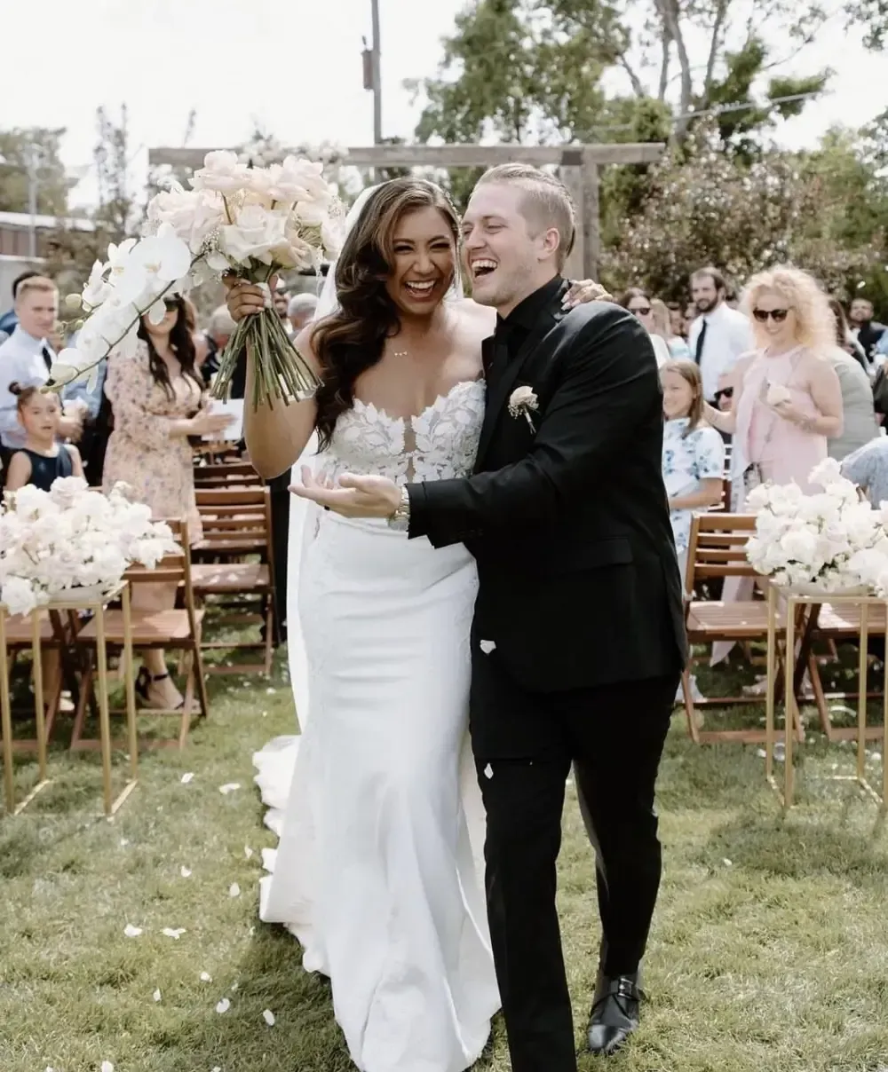 Bride and groom walking, celebrating after wedding ceremony; sunny outdoor setting.