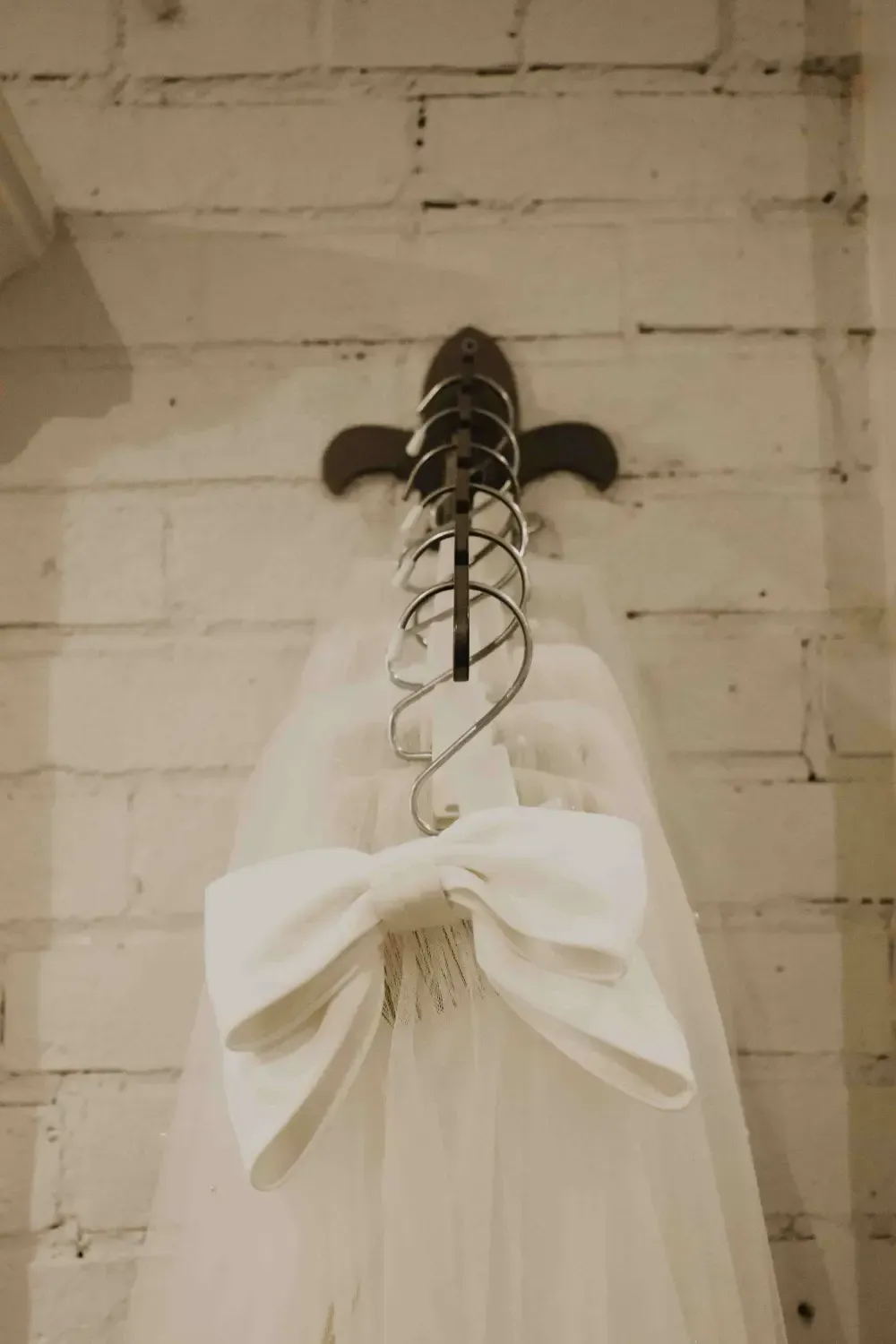 White veil with large bow hanging on a wall-mounted metal rack.