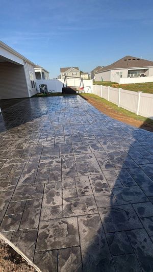 Stamped concrete driveway beside houses, with a white fence and bright blue sky.