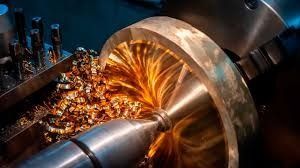 Mecanizado de una pieza metálica en un torno; virutas doradas se desprenden en espiral de la pieza giratoria.