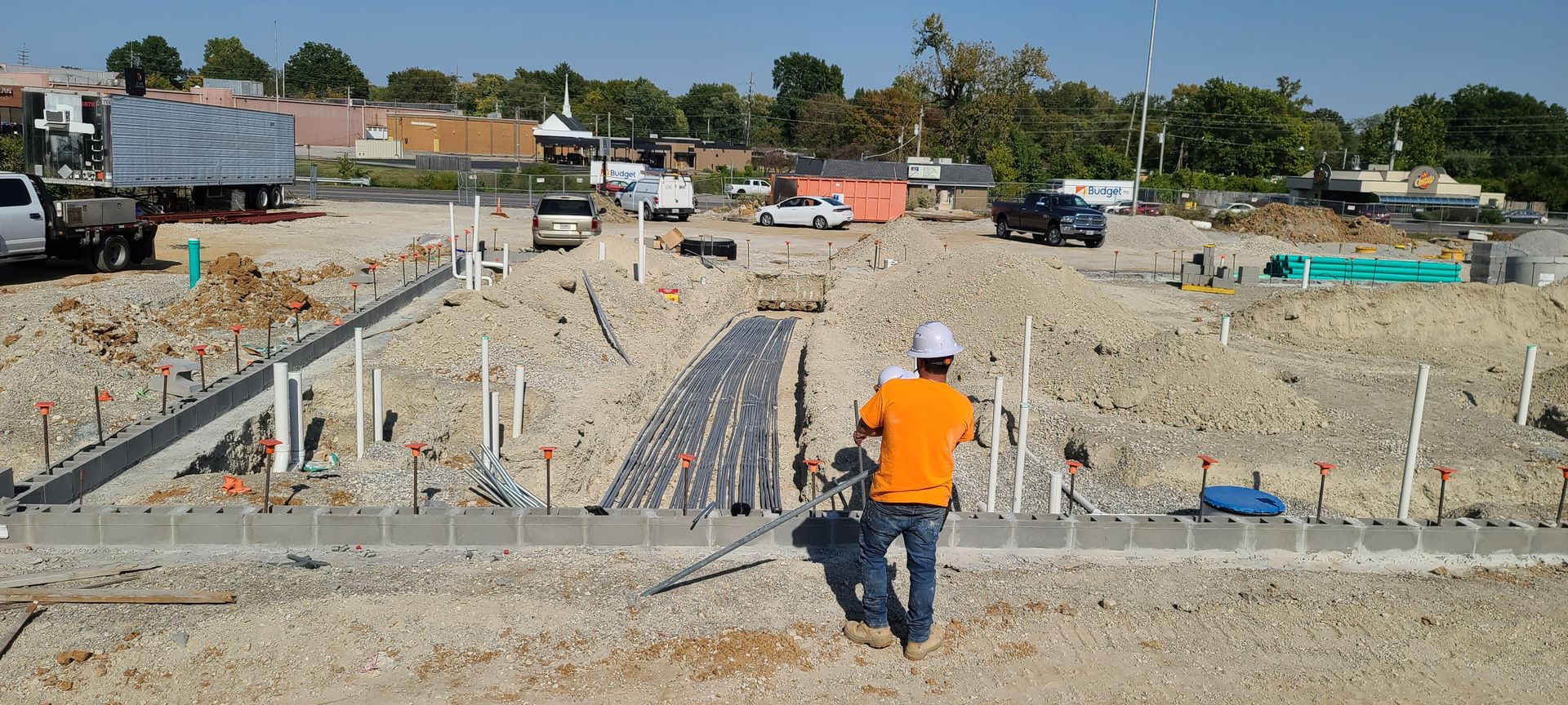 A man in an orange shirt and hard hat is standing in a construction site.