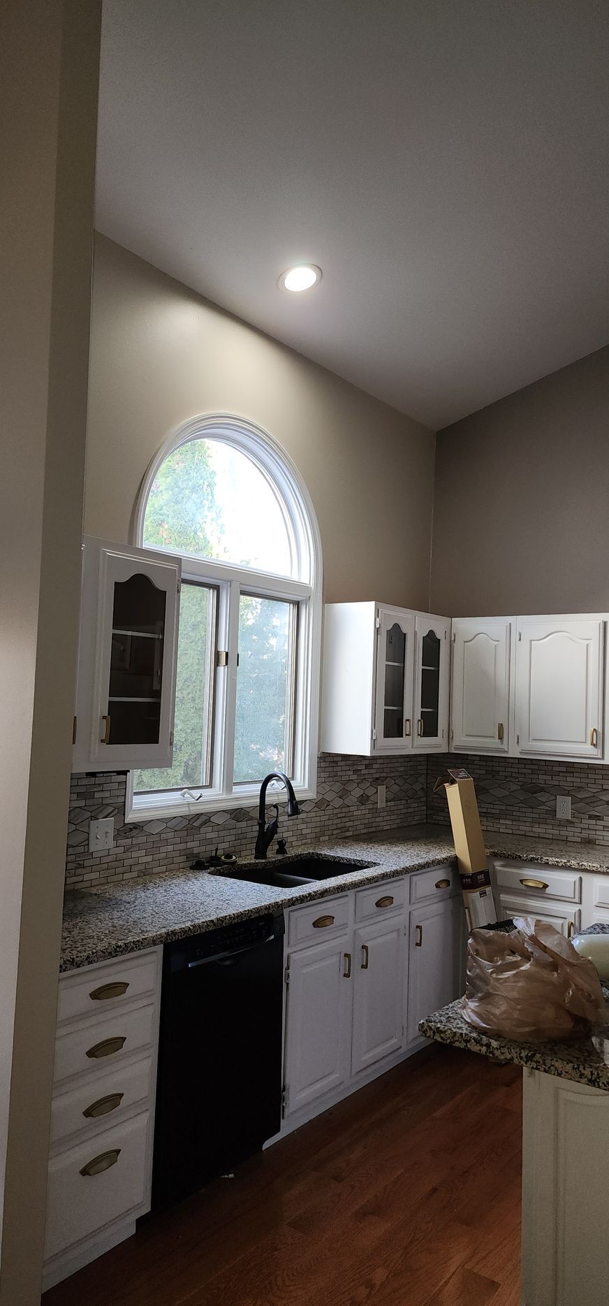 A kitchen with white cabinets , granite counter tops , a sink , and a large window.