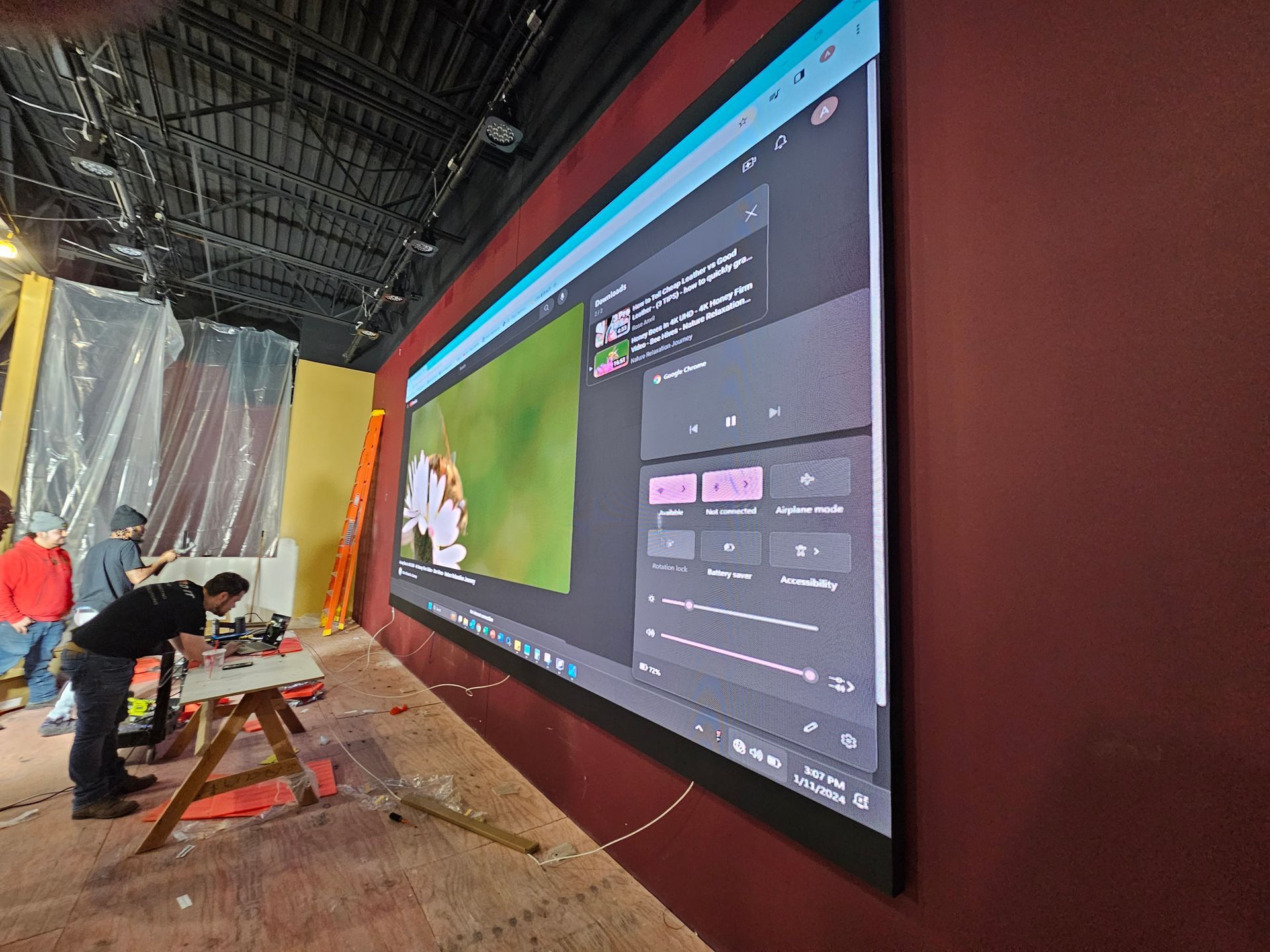 A man is working on a large screen on a wall.