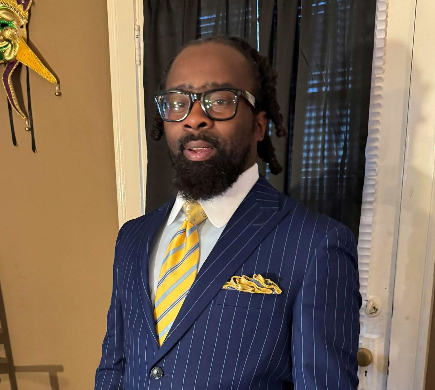 A man in a blue suit and yellow tie is standing in front of a door.